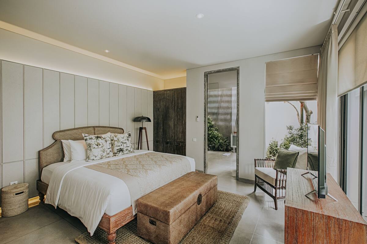 Een moderne slaapkamer met een groot bed, een houten bankje en een bureau met een computer.