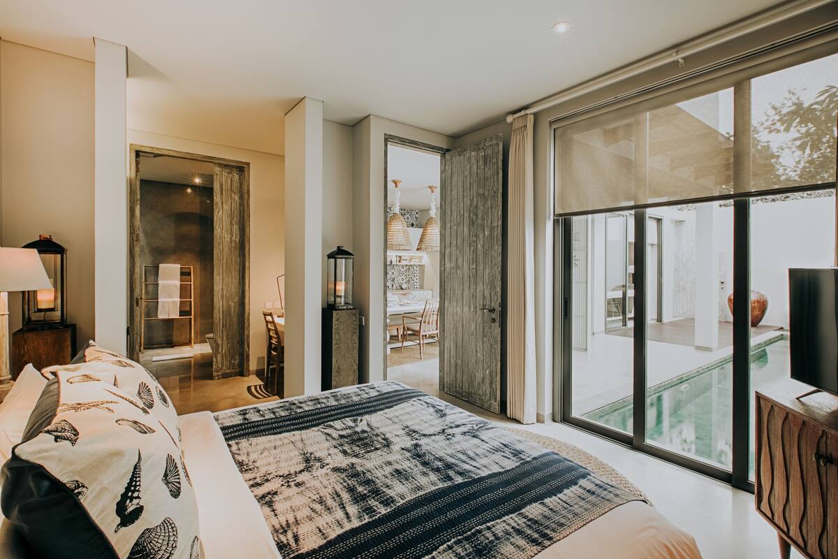 Een moderne slaapkamer met een groot bed, uitzicht op het buitenzwembad en een schuifdeur naar een eetgedeelte.