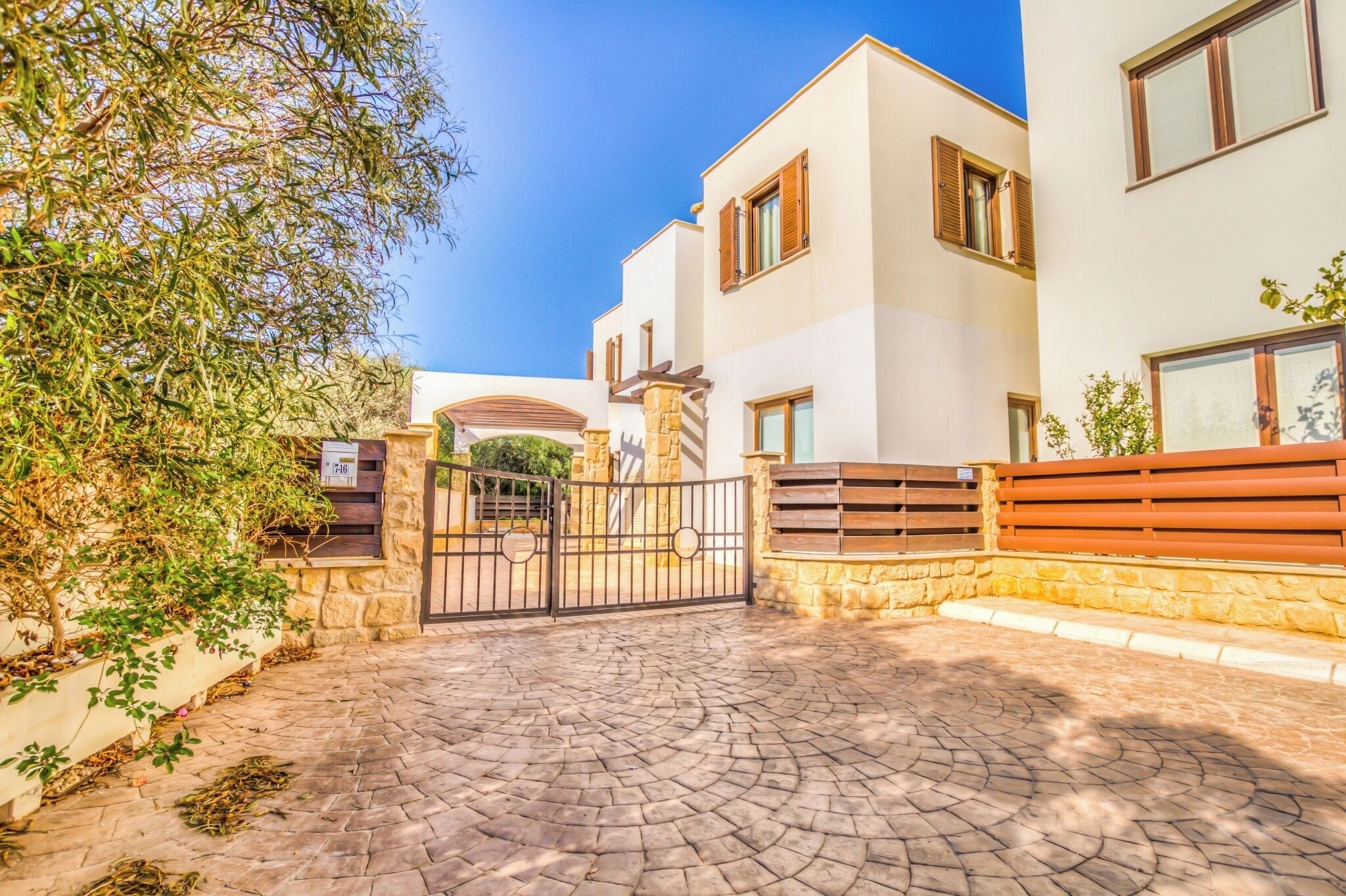 A modern building with a paved entrance, stone walls, and a gated driveway.