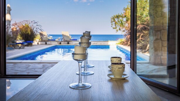 A poolside view with a table featuring wine glasses and coffee cups. - Four Bedroom Front Line (Sea-Front) villa located in an excellent location in the area of Cape Greco (Protaras)