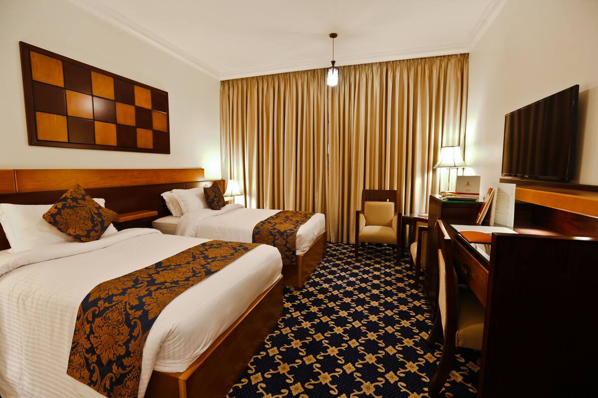 Hotelkamer met twee bedden, een bureau, een stoel, een televisie en een groot raam met gordijnen.