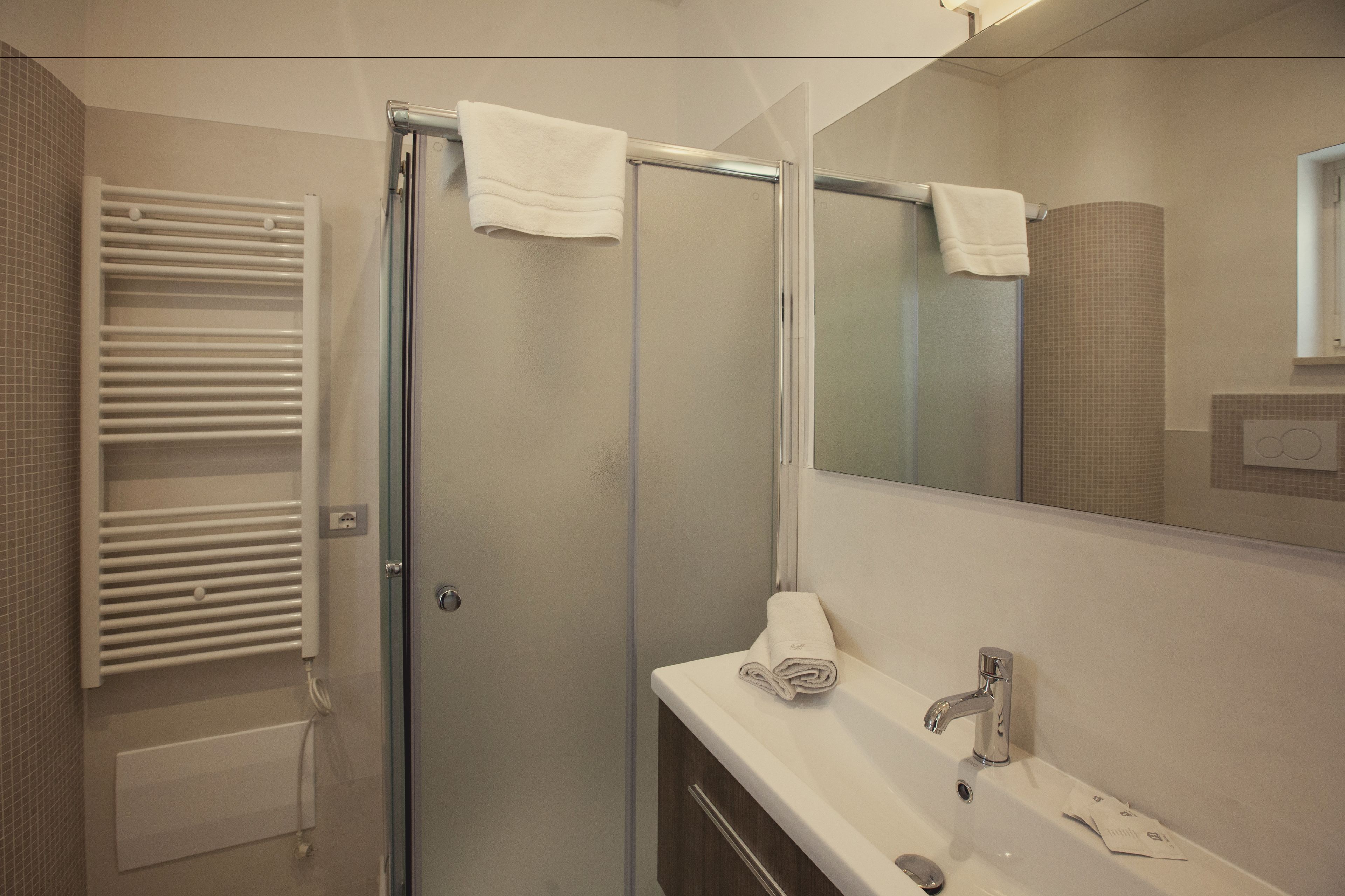 A bathroom with a glass shower door, a white towel on the door, a sink with a mirror, and a towel rack.