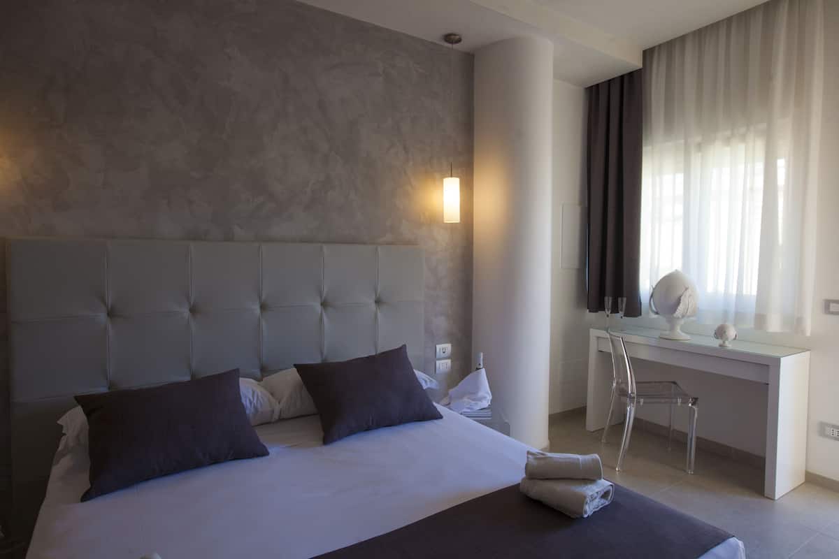 A modern hotel room with a large bed, a desk, and a chair.