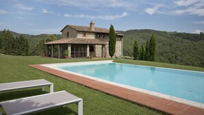 Une villa en pierre dotée d’une piscine, entourée d’une pelouse verdoyante et d’arbres, le tout situé dans un cadre vallonné.