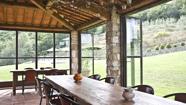 Un espace extérieur abrité, aménagé pour les repas, avec une longue table en bois, plusieurs chaises et un pilier en pierre.