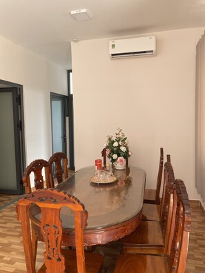 A dining area with a round wooden table, chairs, a vase with flowers, and an air conditioning unit on the wall.