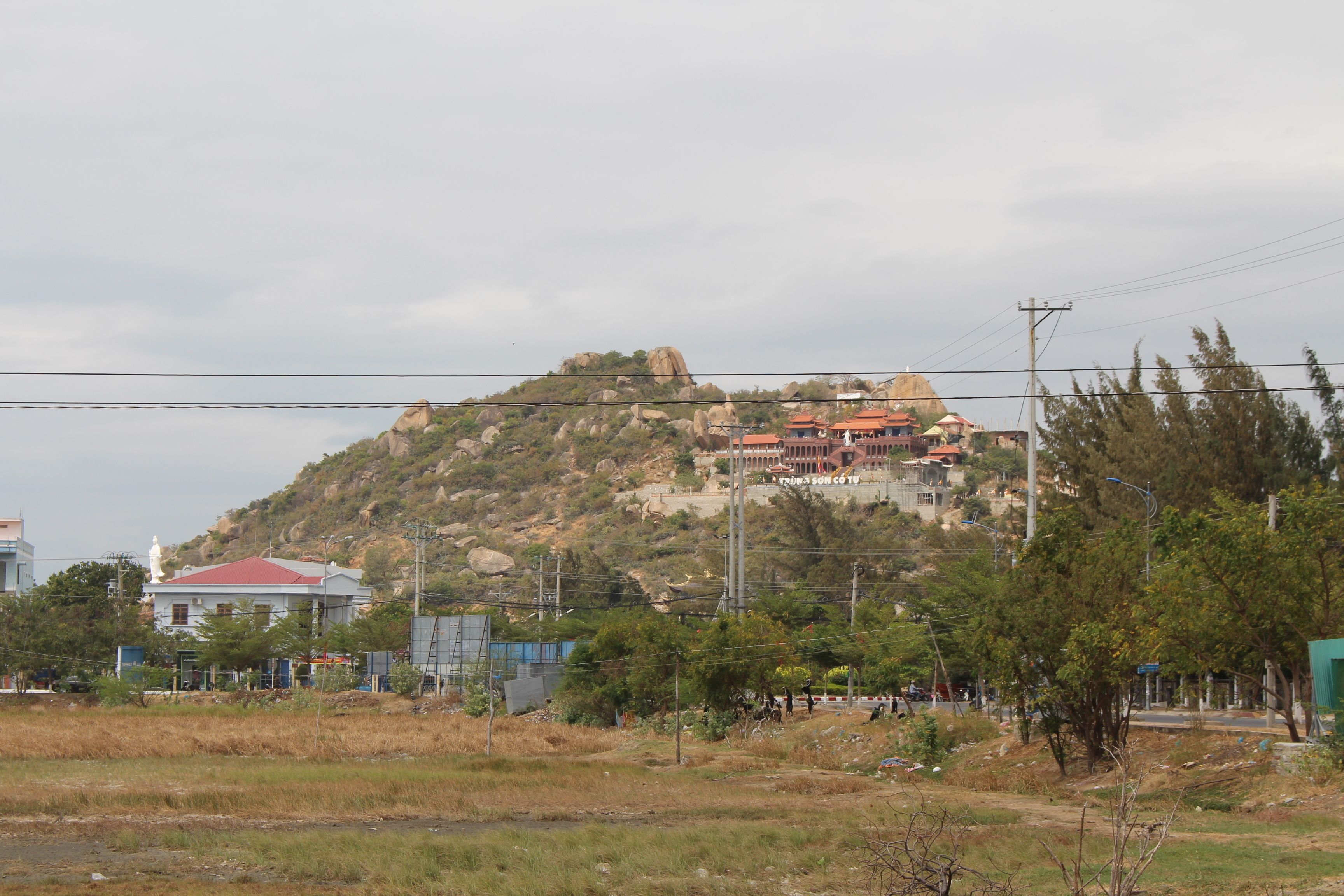 Un edificio en la cima de una colina con techo rojo, rodeado de árboles y algunas construcciones más pequeñas.