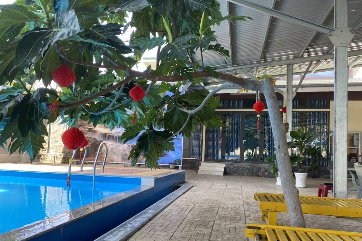 Zona de piscina con suelo de baldosas, sillas reclinables amarillas y un área de estar cubierta con vistas a la piscina.