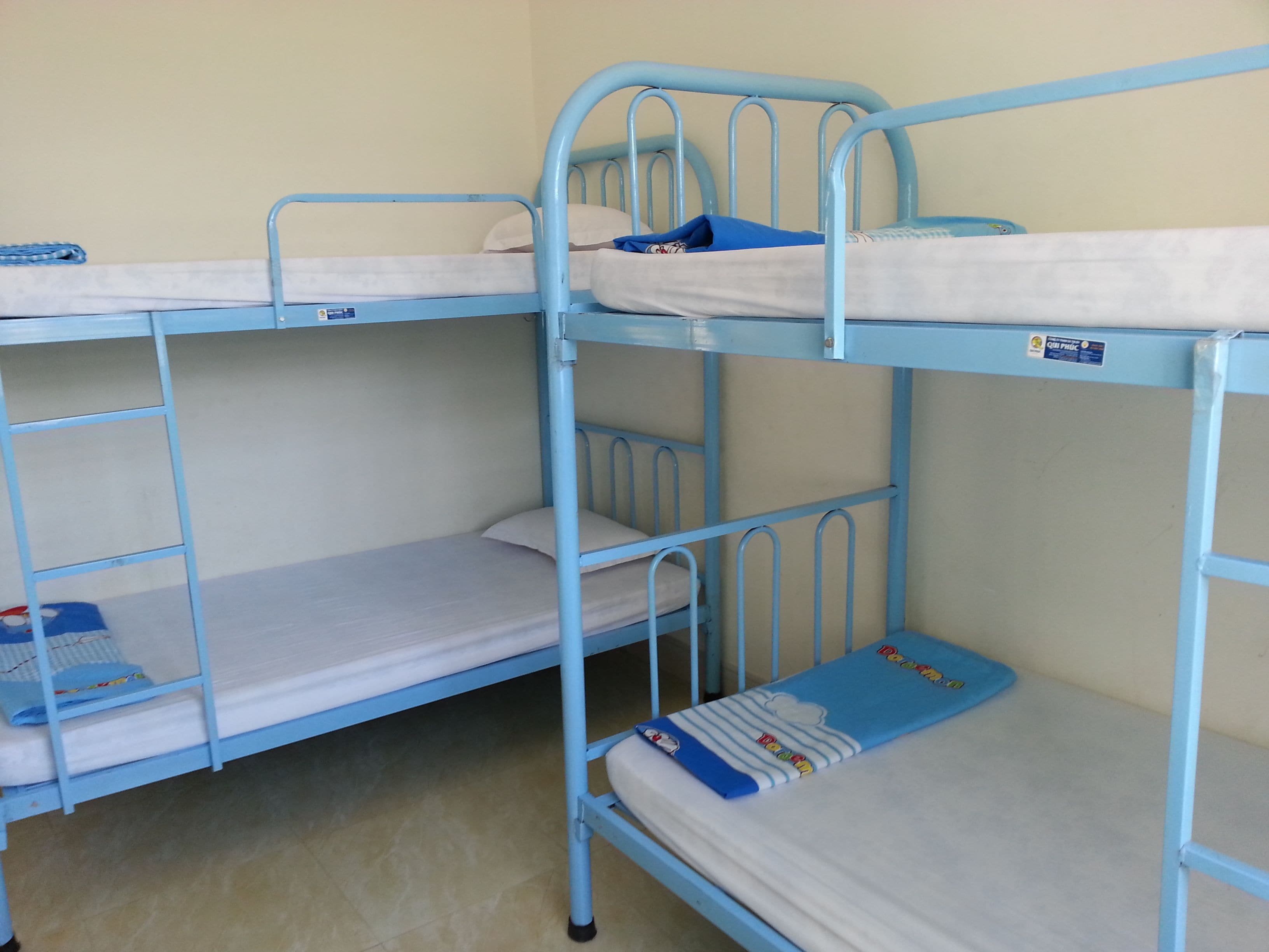 A bunk bed room with a blue metal frame, white bedding, and a blue blanket on the lower bunk.