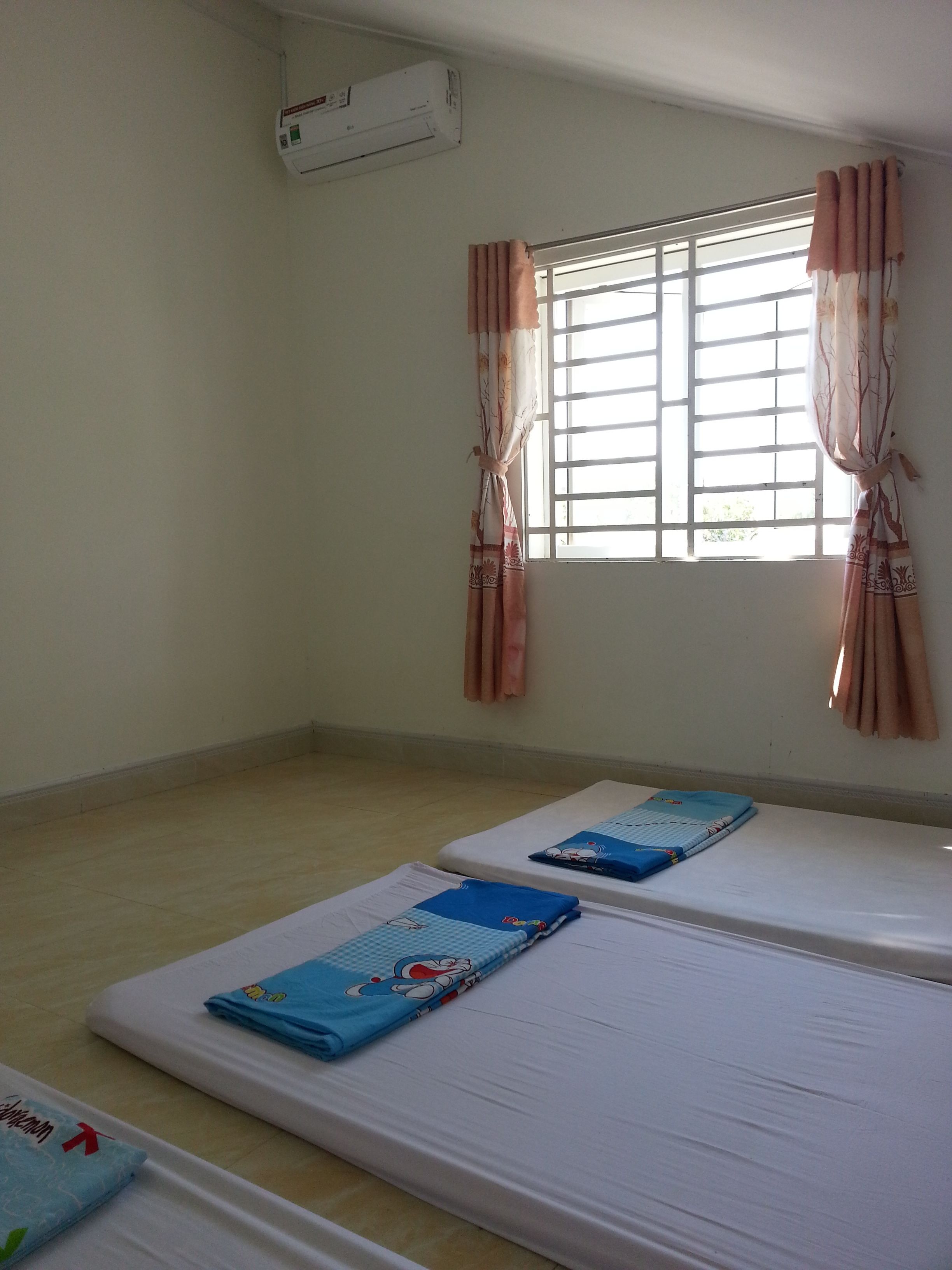 A room with two single beds, a window with curtains, and an air conditioning unit.