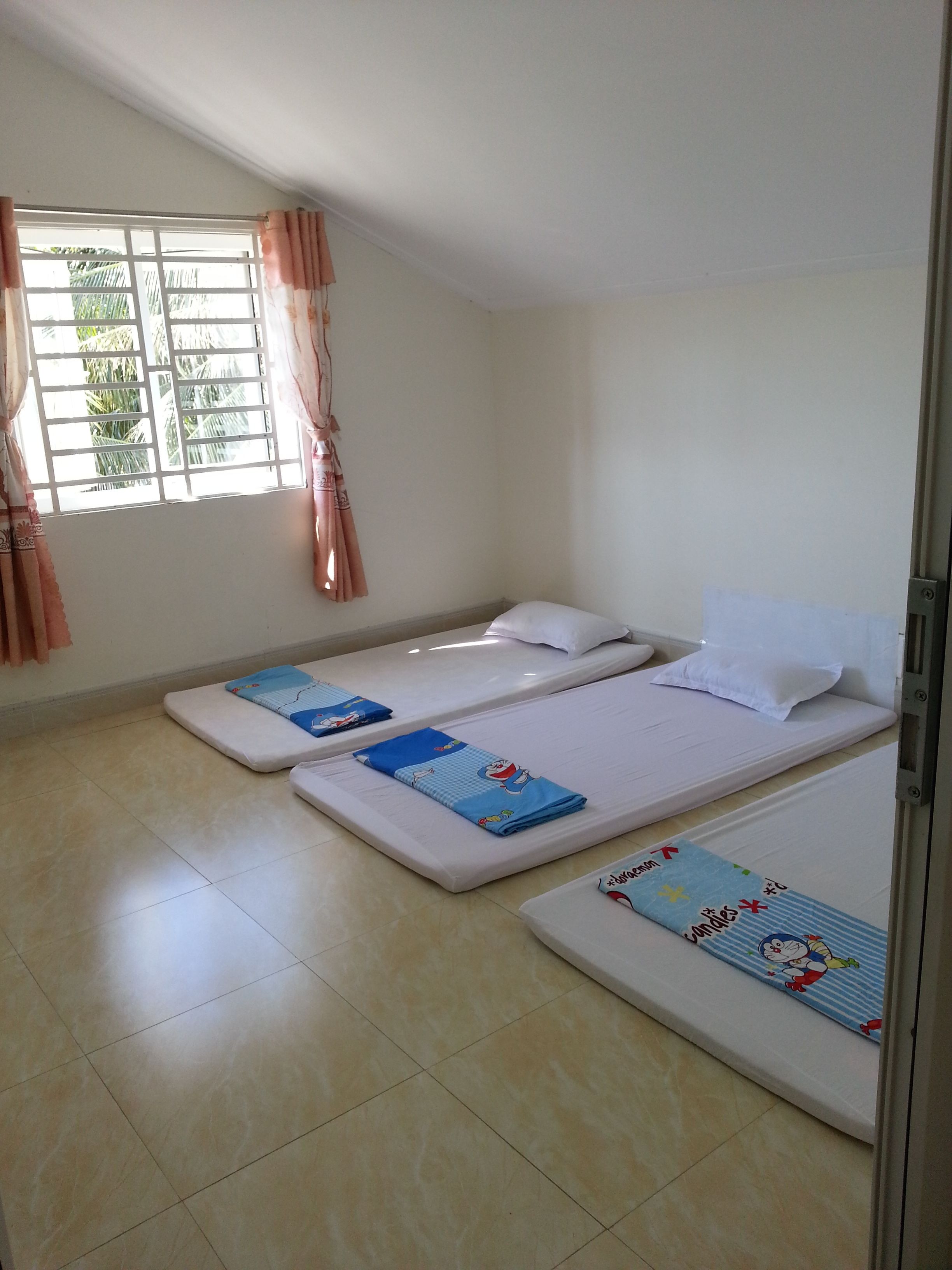 A room with two single beds, a window with curtains, and a tiled floor.