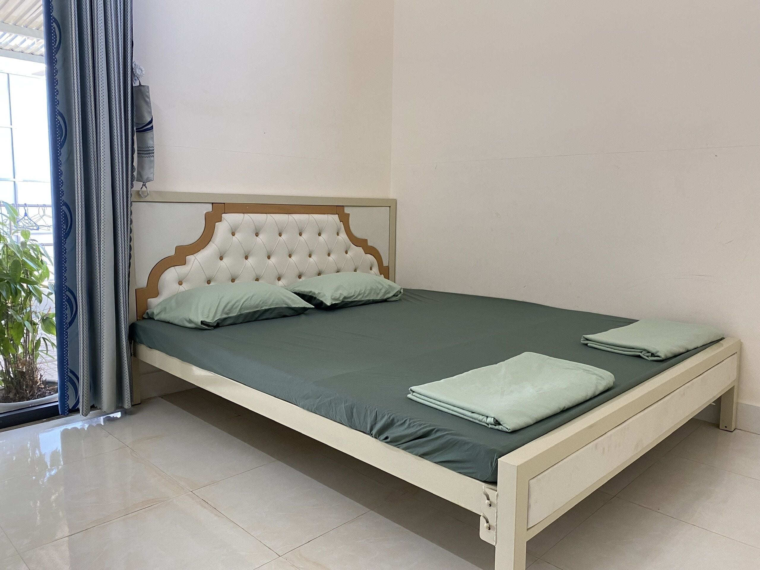 A neatly made bed with a tufted headboard, a green bedspread, and two pillows.