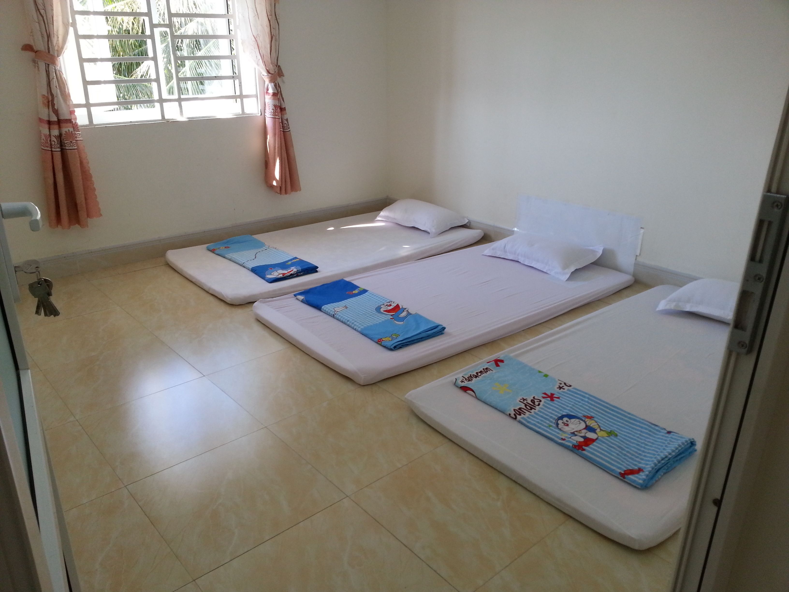 Une chambre avec deux lits simples, chacun équipé d’un matelas et d’un oreiller, et une petite fenêtre avec des rideaux.