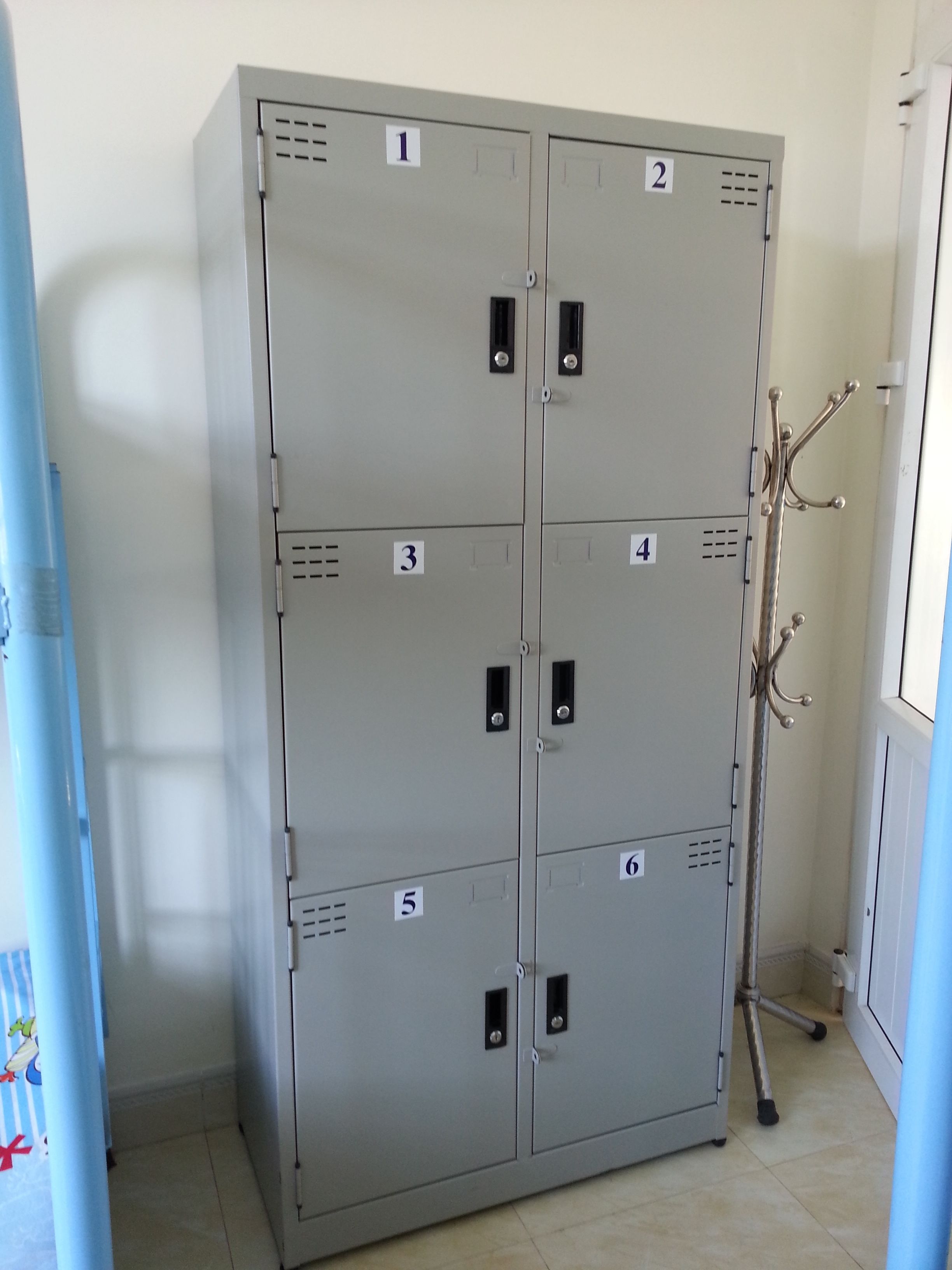 A set of six grey metal lockers with numbered doors, a coat rack, and a blue curtain with cartoon characters.