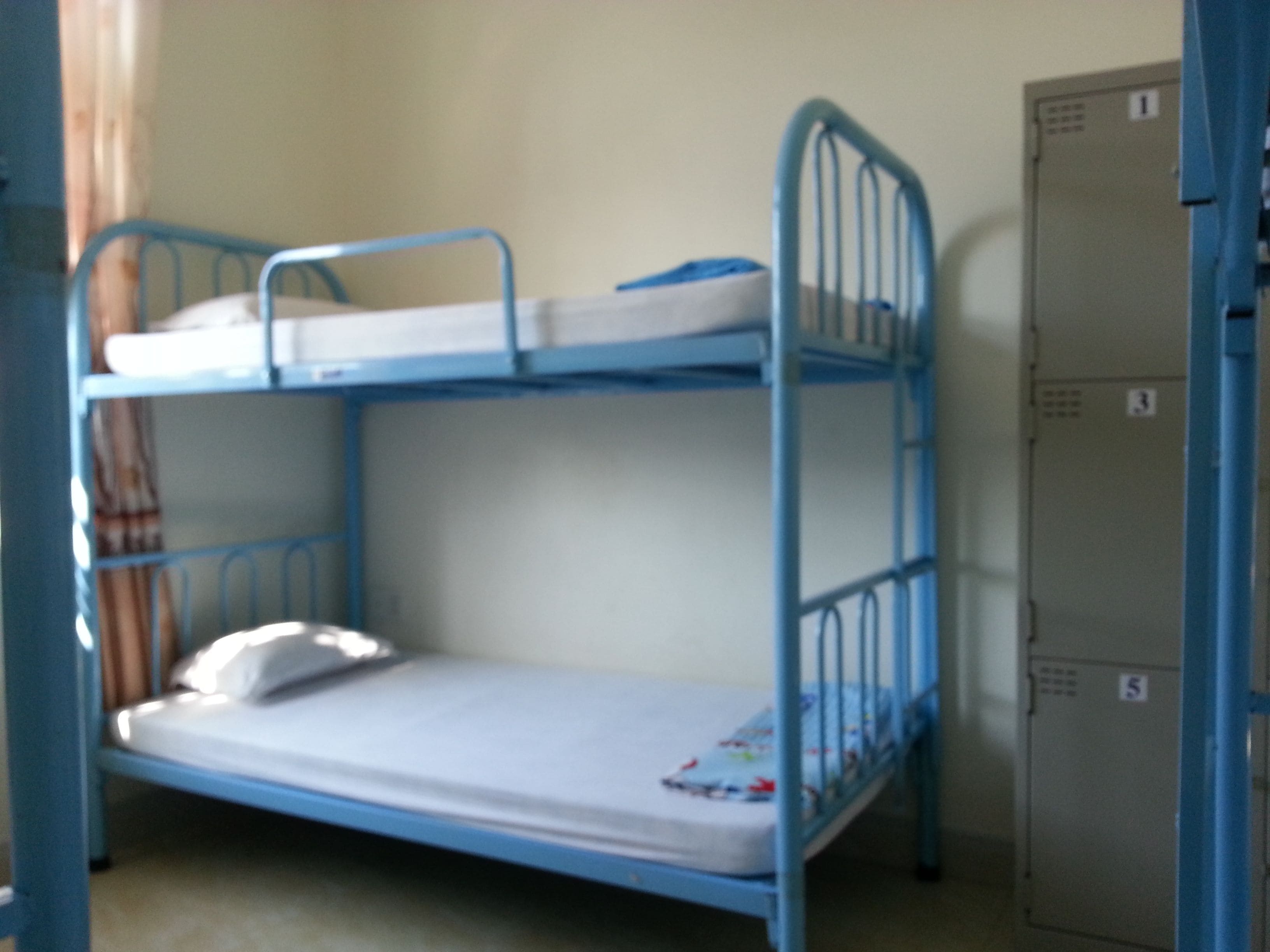 A bunk bed with a mattress and pillows, a metal wardrobe, and a number sign on the wardrobe.