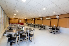 A spacious dining area with multiple tables and chairs, air conditioning units, and a red carpet leading to a stage.