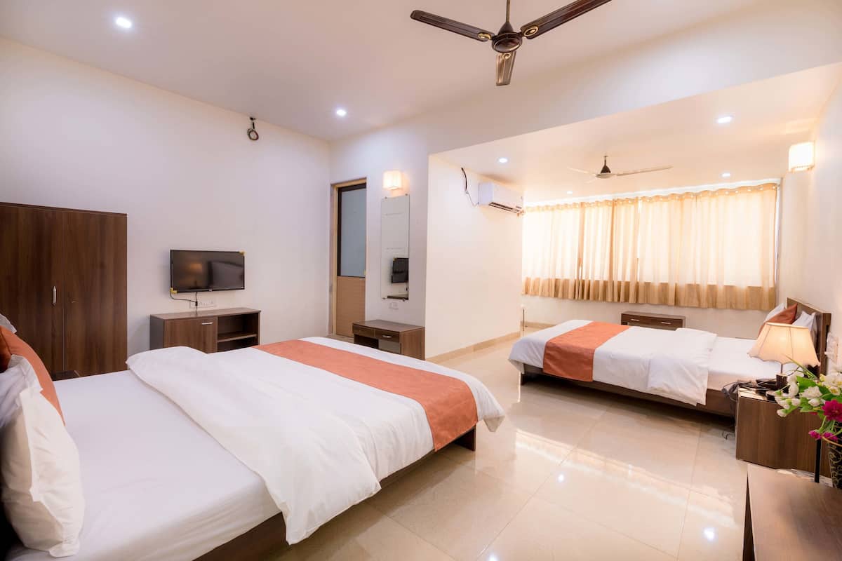 A hotel room with two beds, a TV, a wardrobe, a desk, and a ceiling fan.
