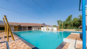 Una piscina con cubierta a cuadros, un edificio de techo rojo y una montaña al fondo.