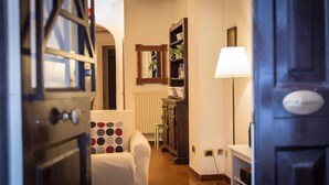 A hallway with a white armchair, a mirror, a lamp, and a wooden cabinet.