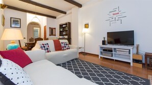 A living room with a sofa, a TV, and a wall with multilingual welcome signs.