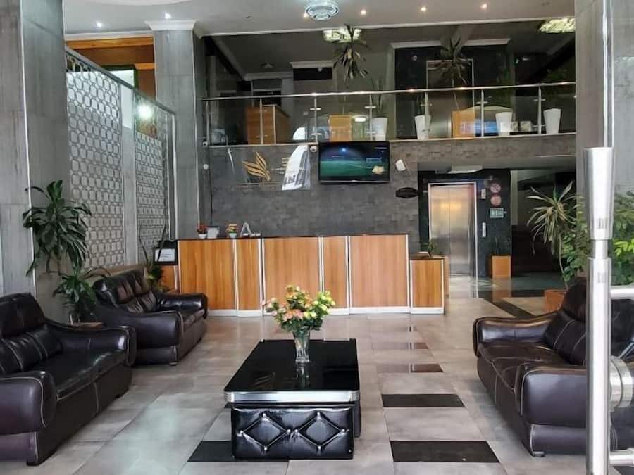 Um hall moderno com um candelabro, sofás de couro, um balcão de recepção e uma tela de televisão.