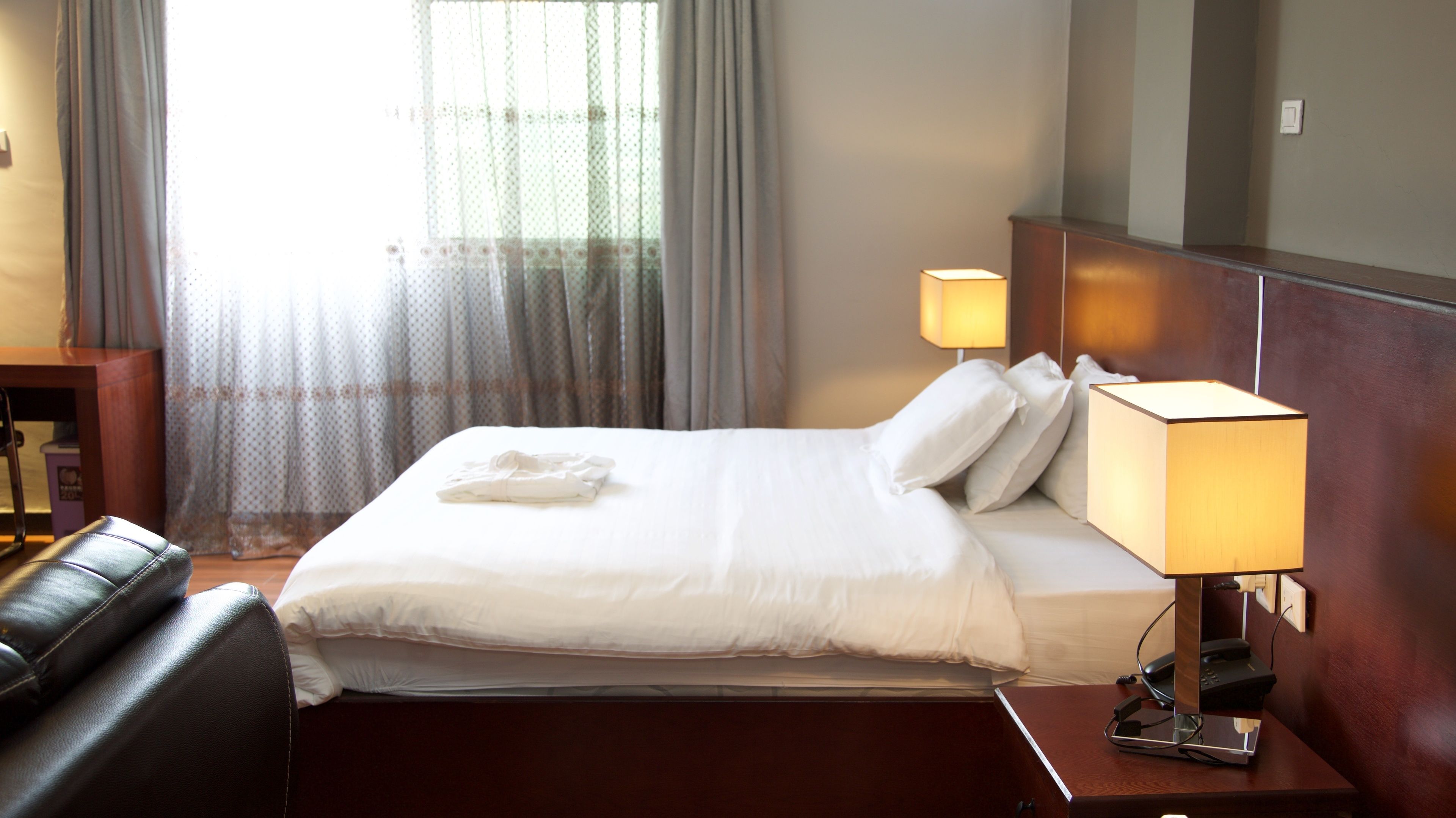 Una habitación de hotel con una cama bien hecha, una lámpara de noche, un mesita de madera y un sillón de cuero.
