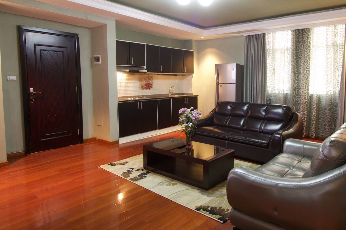 A living room with a sofa, coffee table, and a kitchen area with cabinets and a stove.