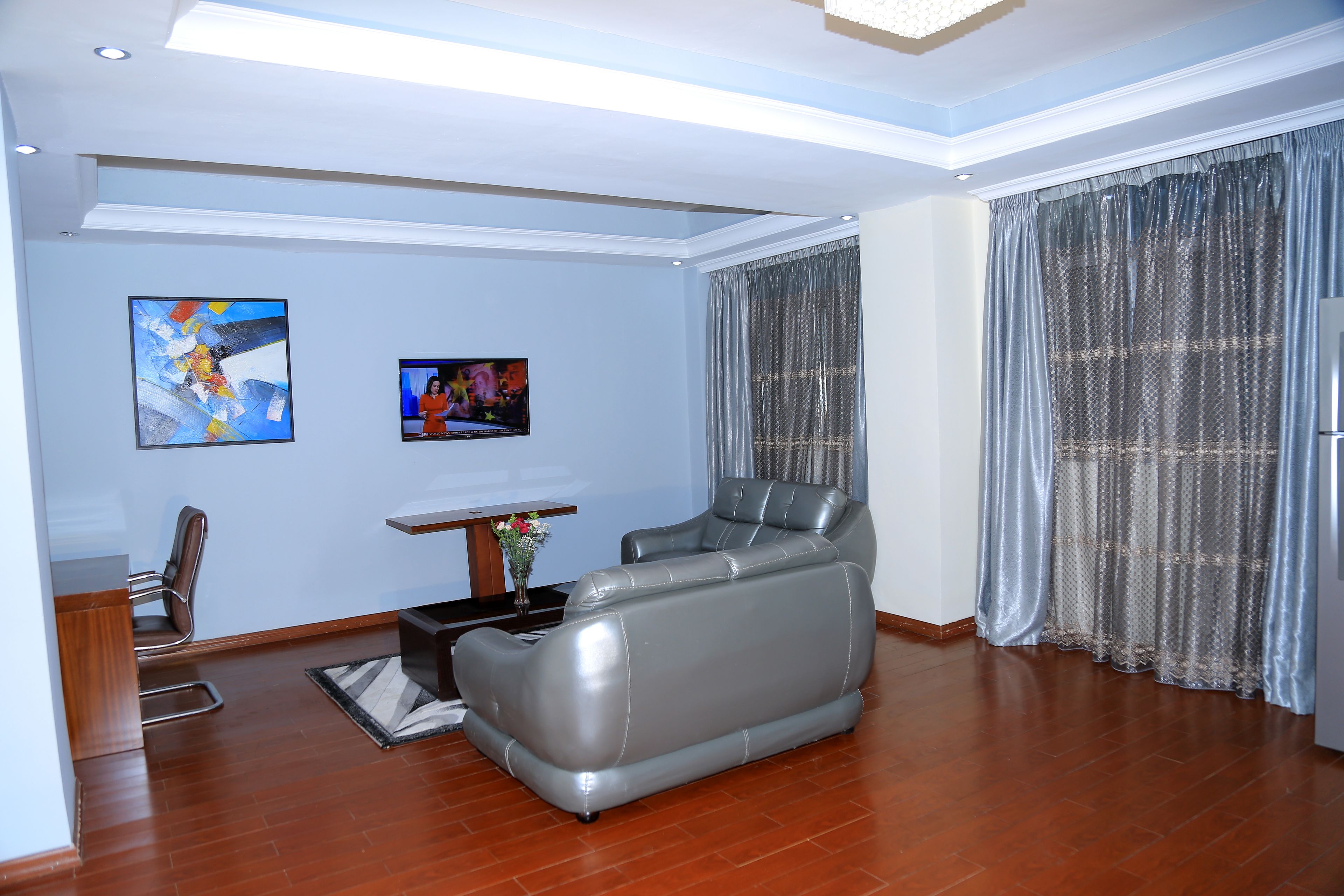 A modern living room with a grey leather sofa, a small table with a vase, and two framed pictures on the wall.