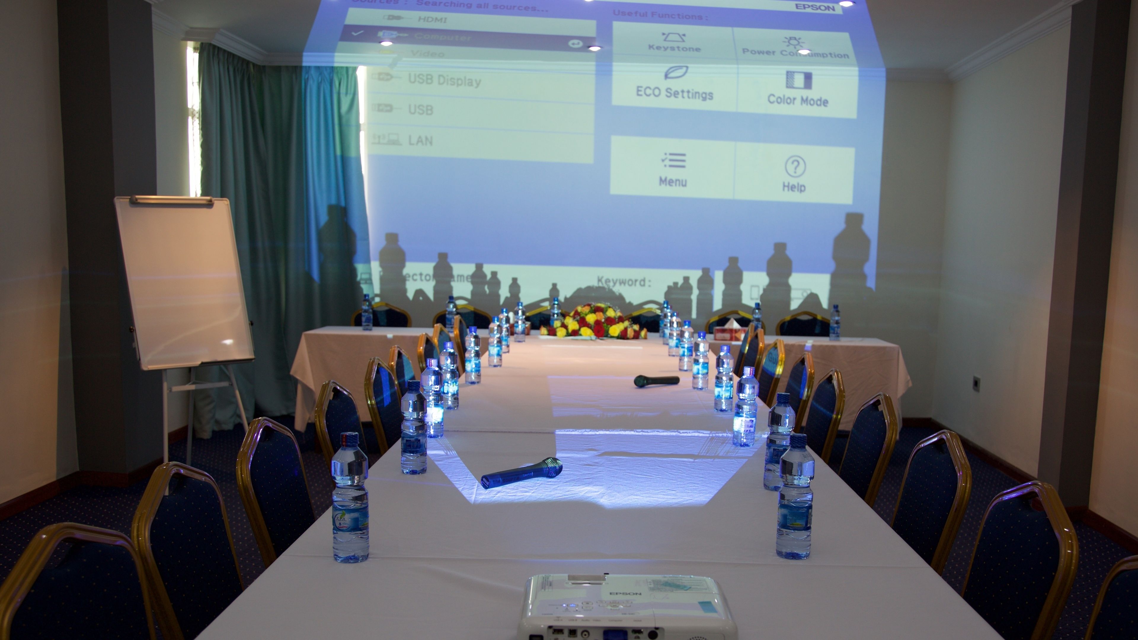 Une salle de conférence avec une longue table, des chaises, des bouteilles d’eau et un écran de projection sur lequel est affichée une présentation.