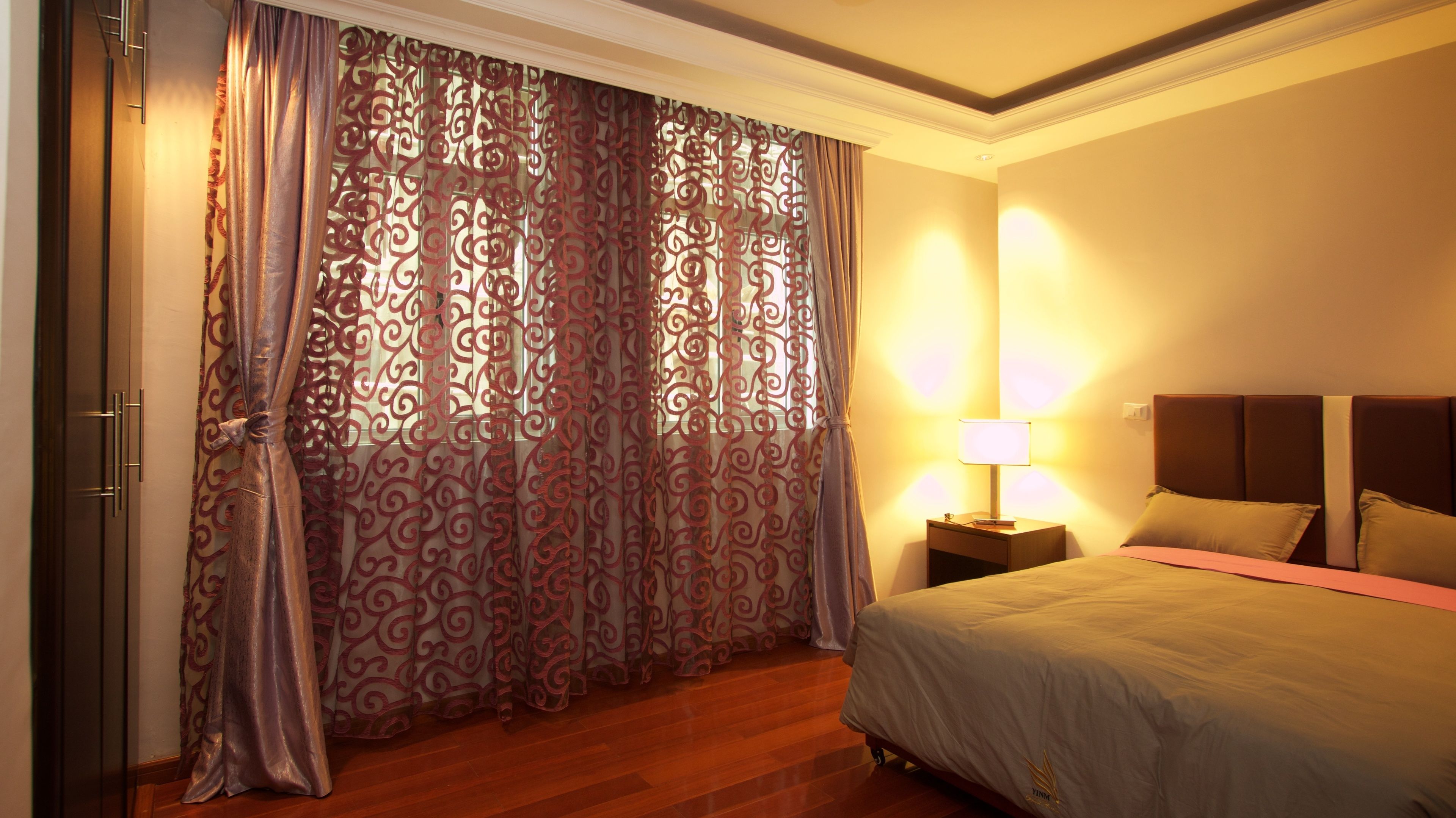 A hotel room with a bed, a nightstand with a lamp, and a curtain with a red pattern.