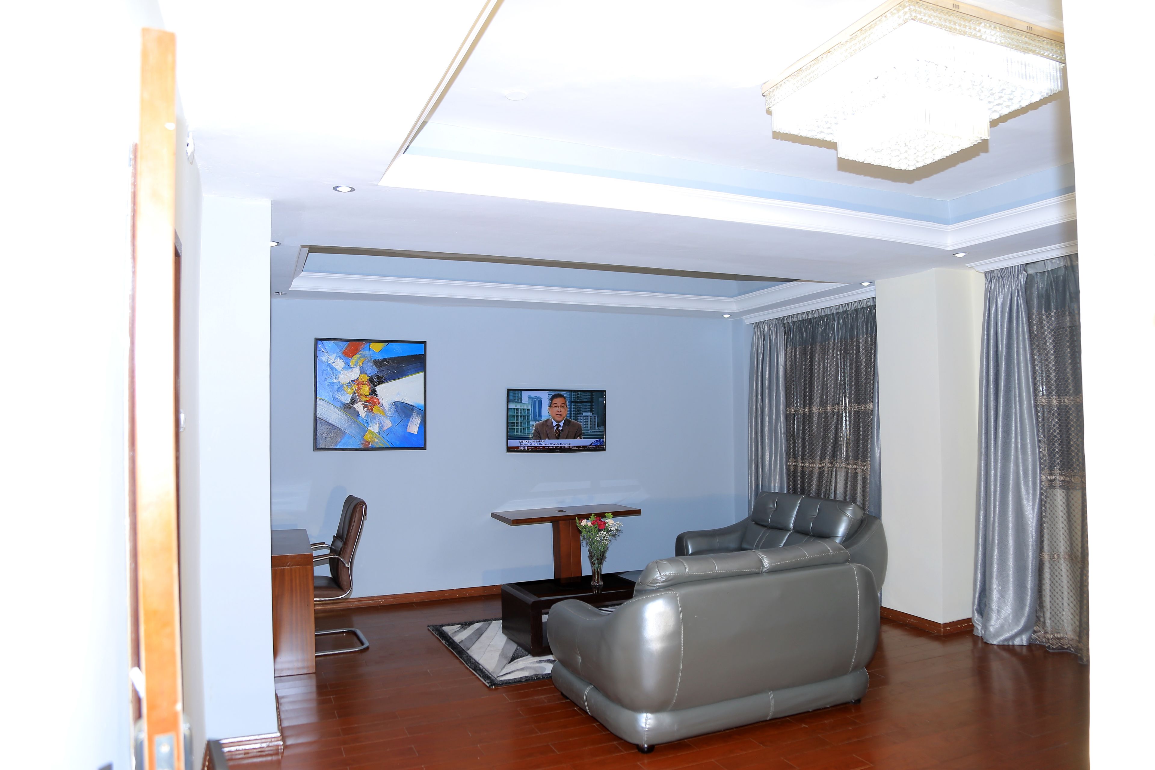 A modern living room with a grey leather sofa, a wooden coffee table, and a flat-screen TV mounted on the wall.