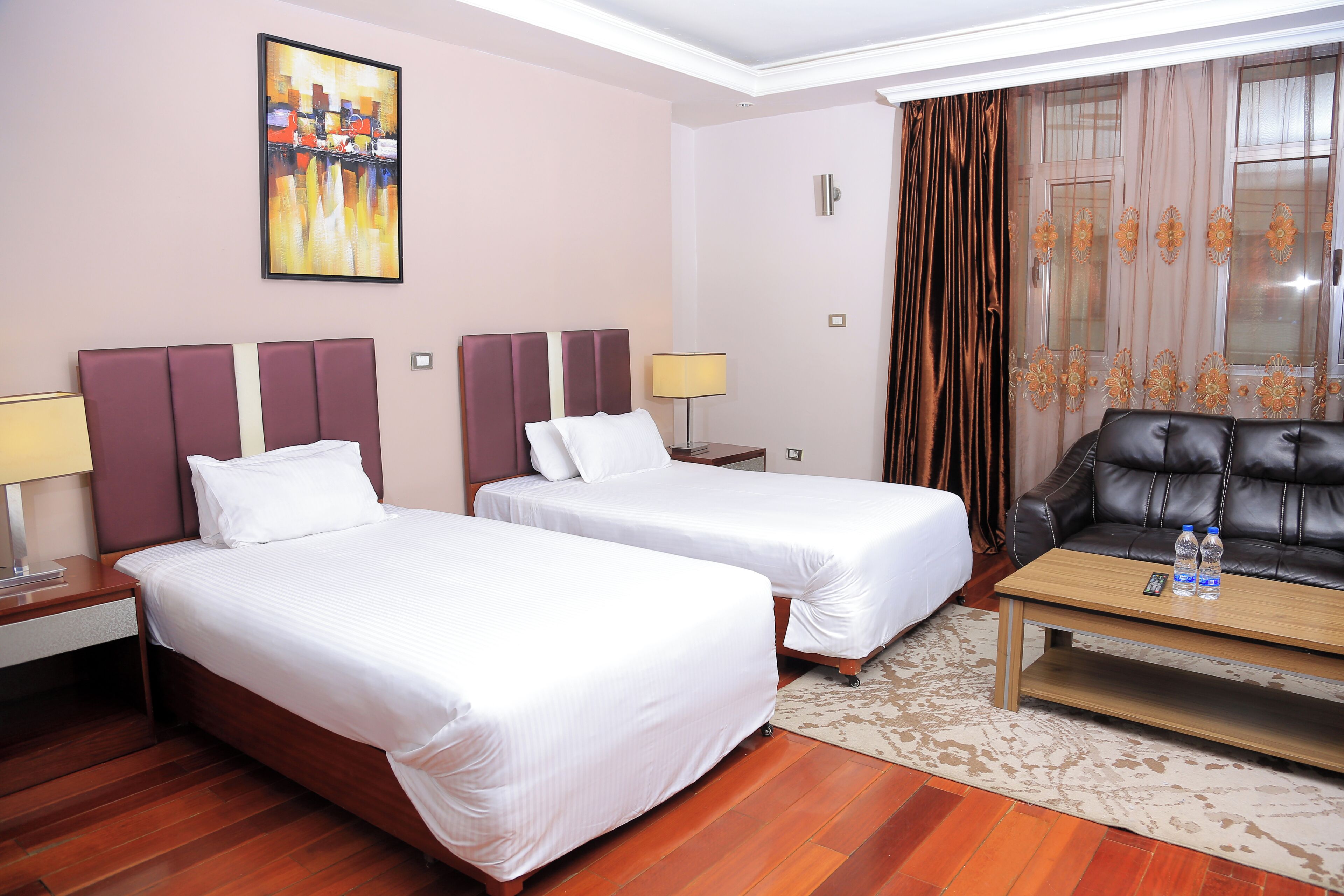 A hotel room with two beds, a sofa, a coffee table, and a painting on the wall.