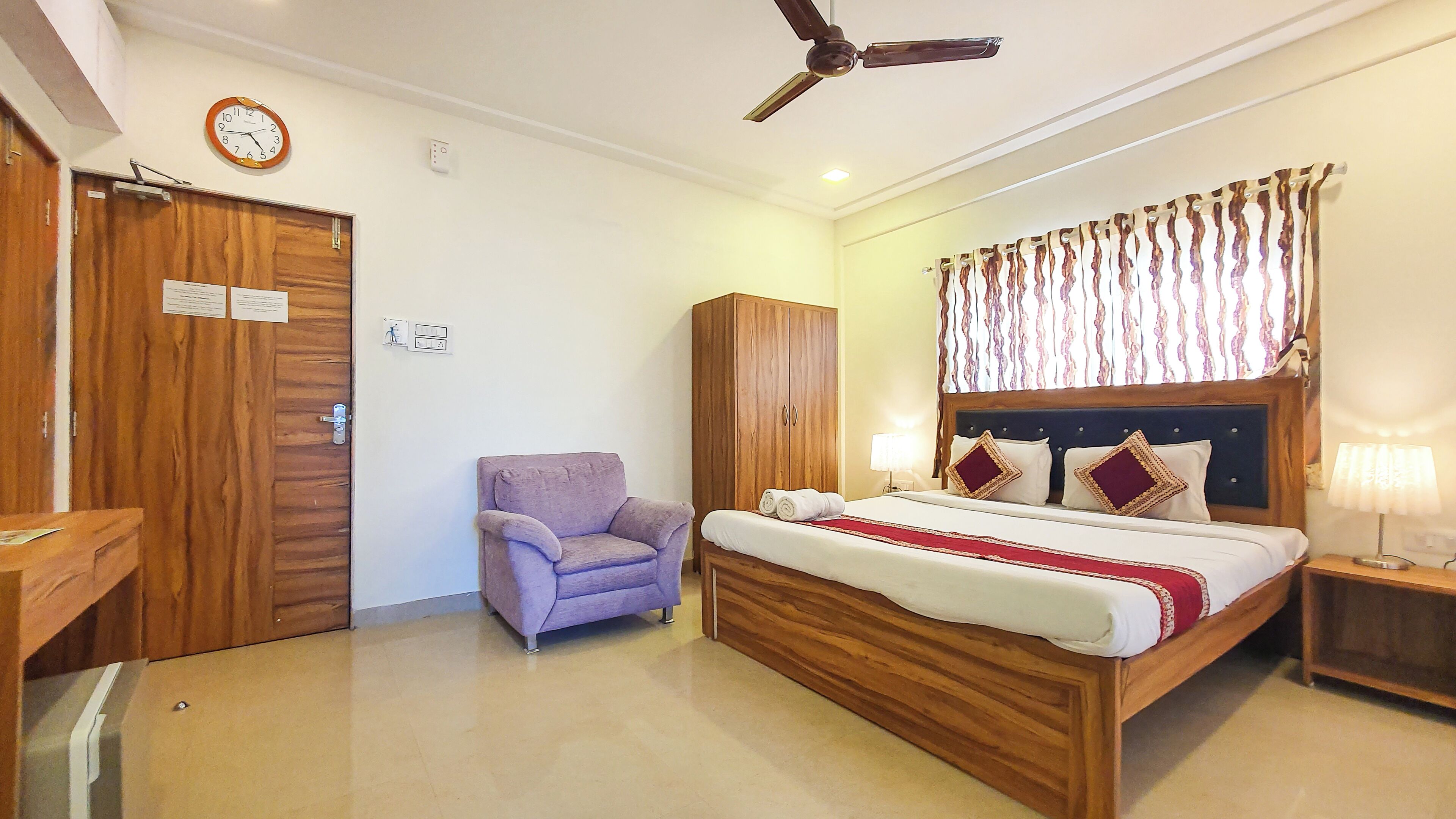 Un dormitorio con una cama de madera, un sillón morado, un armario y un ventilador de techo.