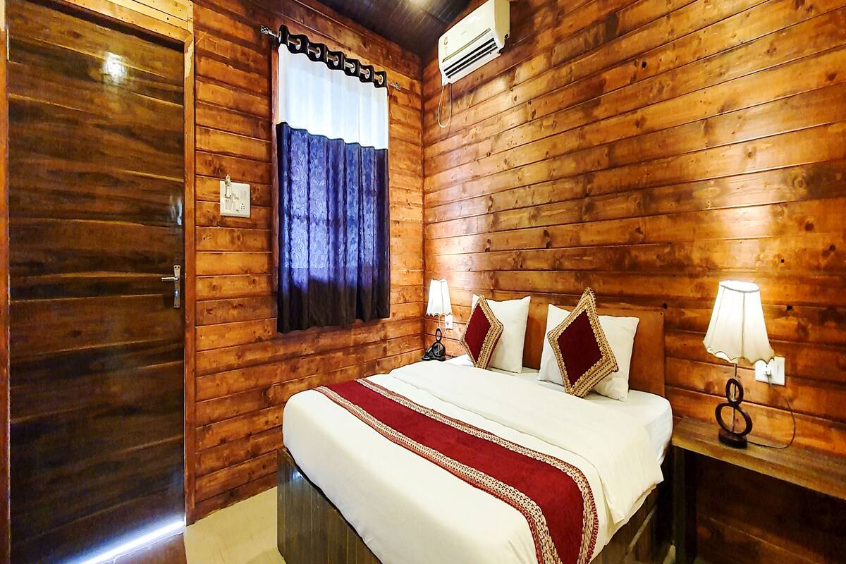A wooden-paneled room with a bed, a nightstand, and a wall-mounted air conditioner.