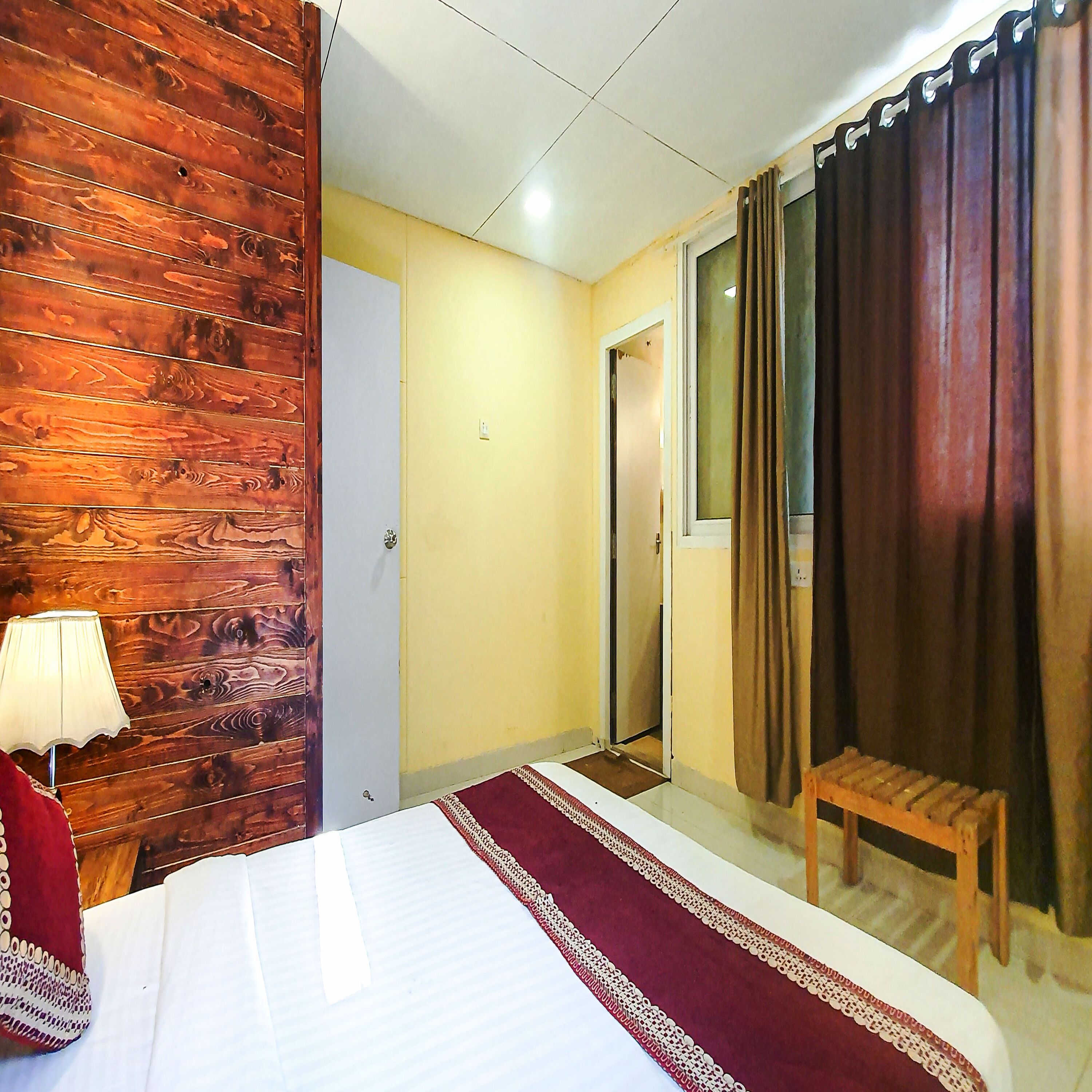 Una camera d'albergo con una parete in legno, un letto con copriletto rosso e bianco, una piccola panca di legno e una lampada.