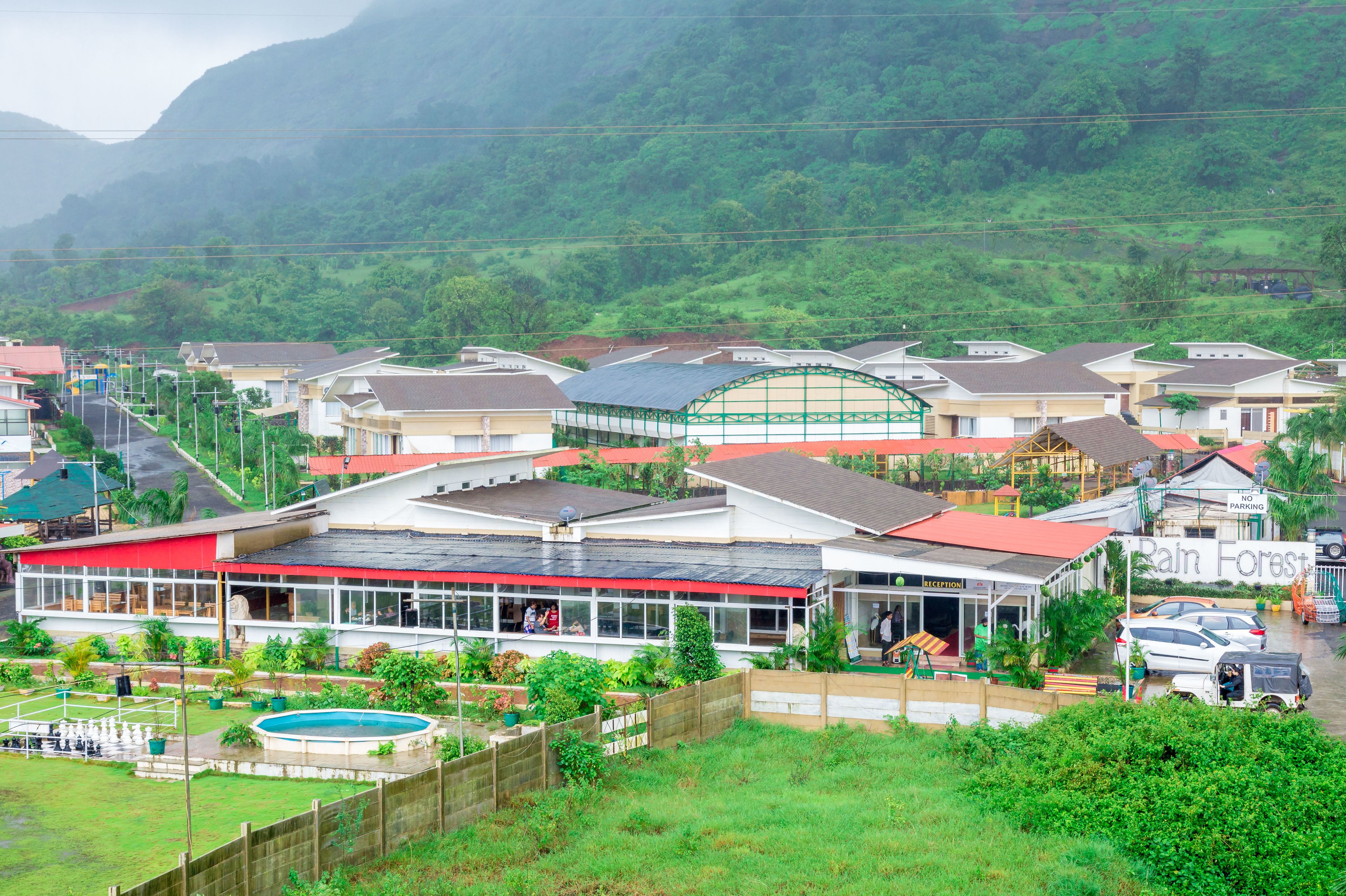 A hotel with a swimming pool, a reception area, and a view of a lush green forest.