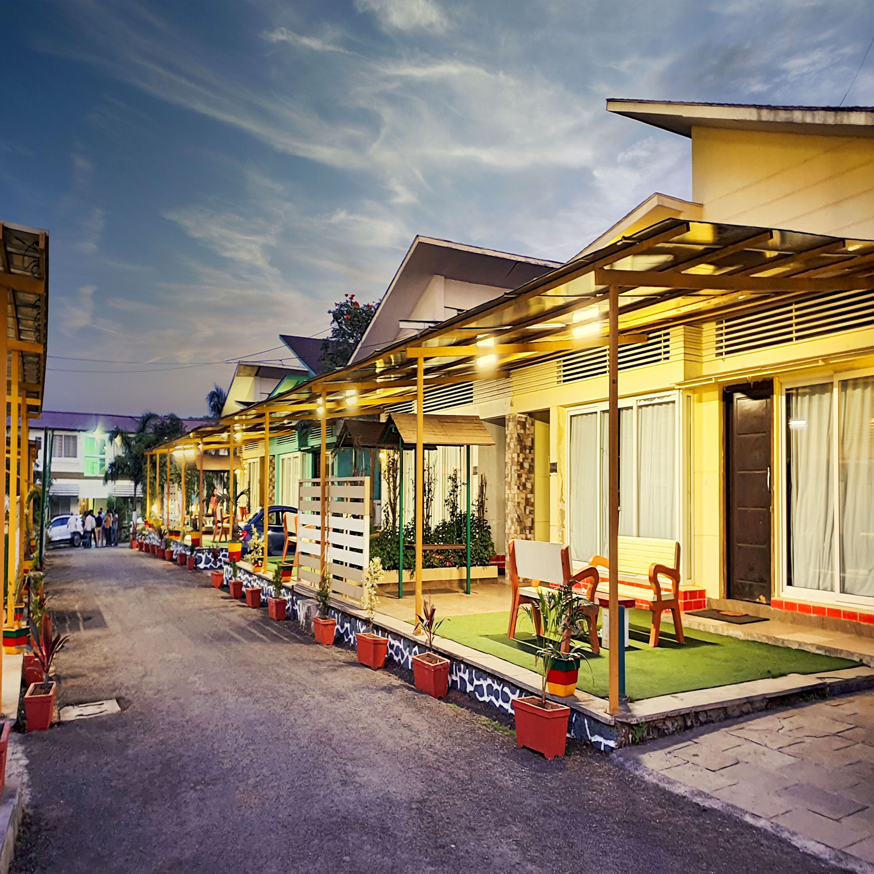 A row of brightly lit, single-story buildings with outdoor seating areas and potted plants.