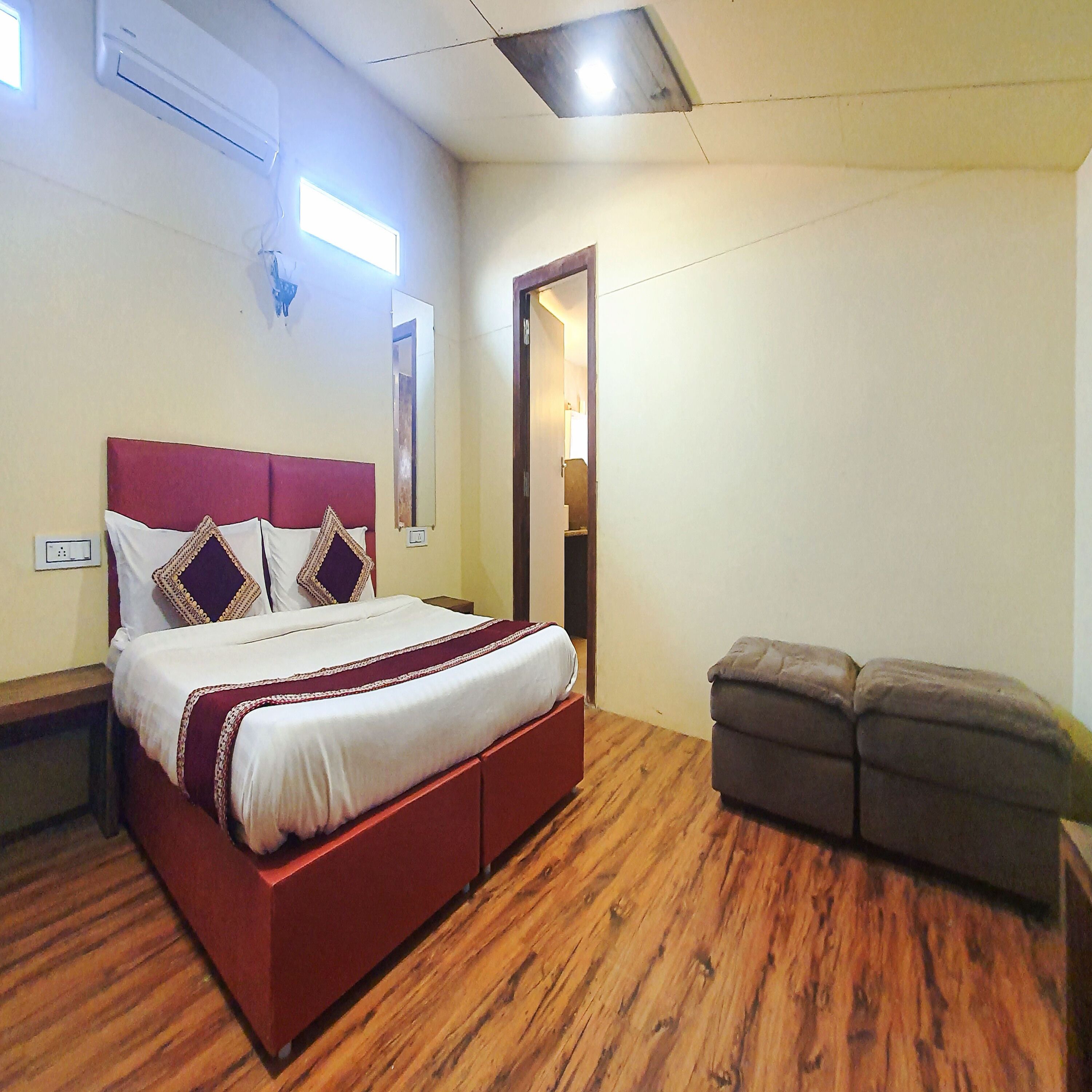 Ein Schlafzimmer mit Holzboden, einem roten Bettgestell, einer weißen Bettdecke und einer kleinen grauen Bank.