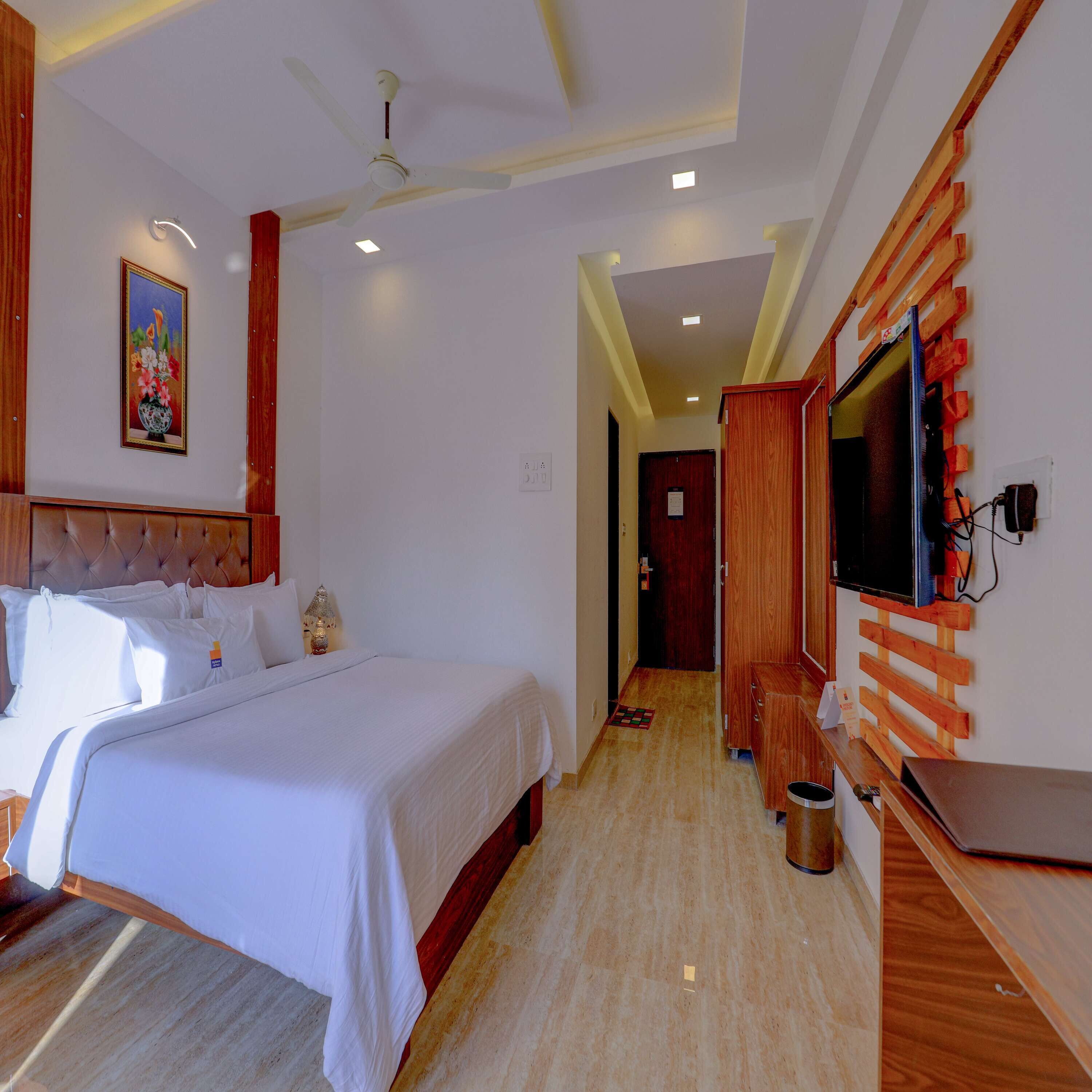 Una habitación de hotel con una cama, un ventilador de techo, un televisor montado en la pared y un armario de madera.
