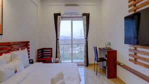 Una habitación de hotel con una cama grande, un escritorio con silla, un televisor montado en la pared y un ventilador de techo.