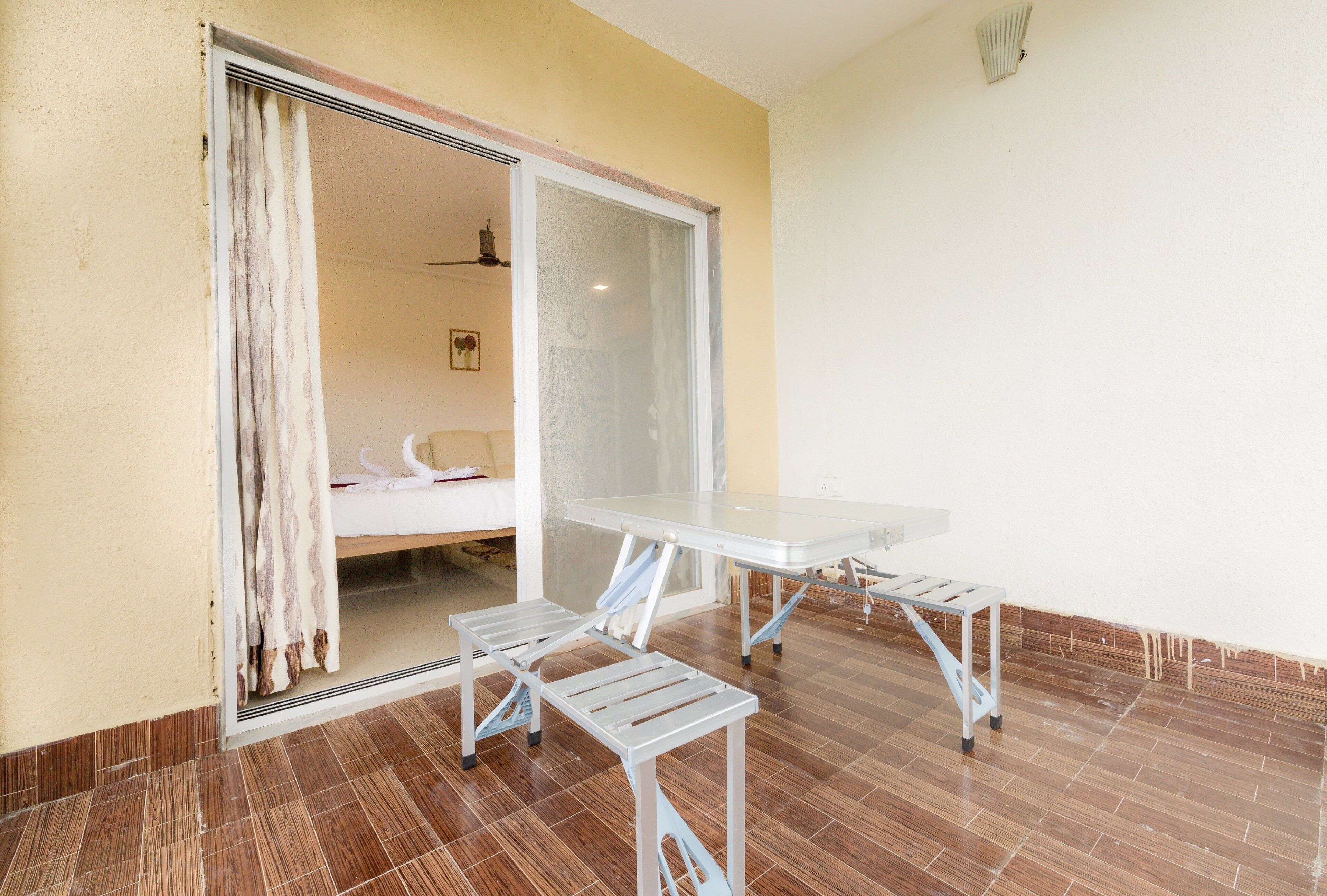 Une pièce dotée d’une porte-fenêtre coulissante donnant sur une chambre, d’une table blanche avec deux chaises et d’un sol carrelé.