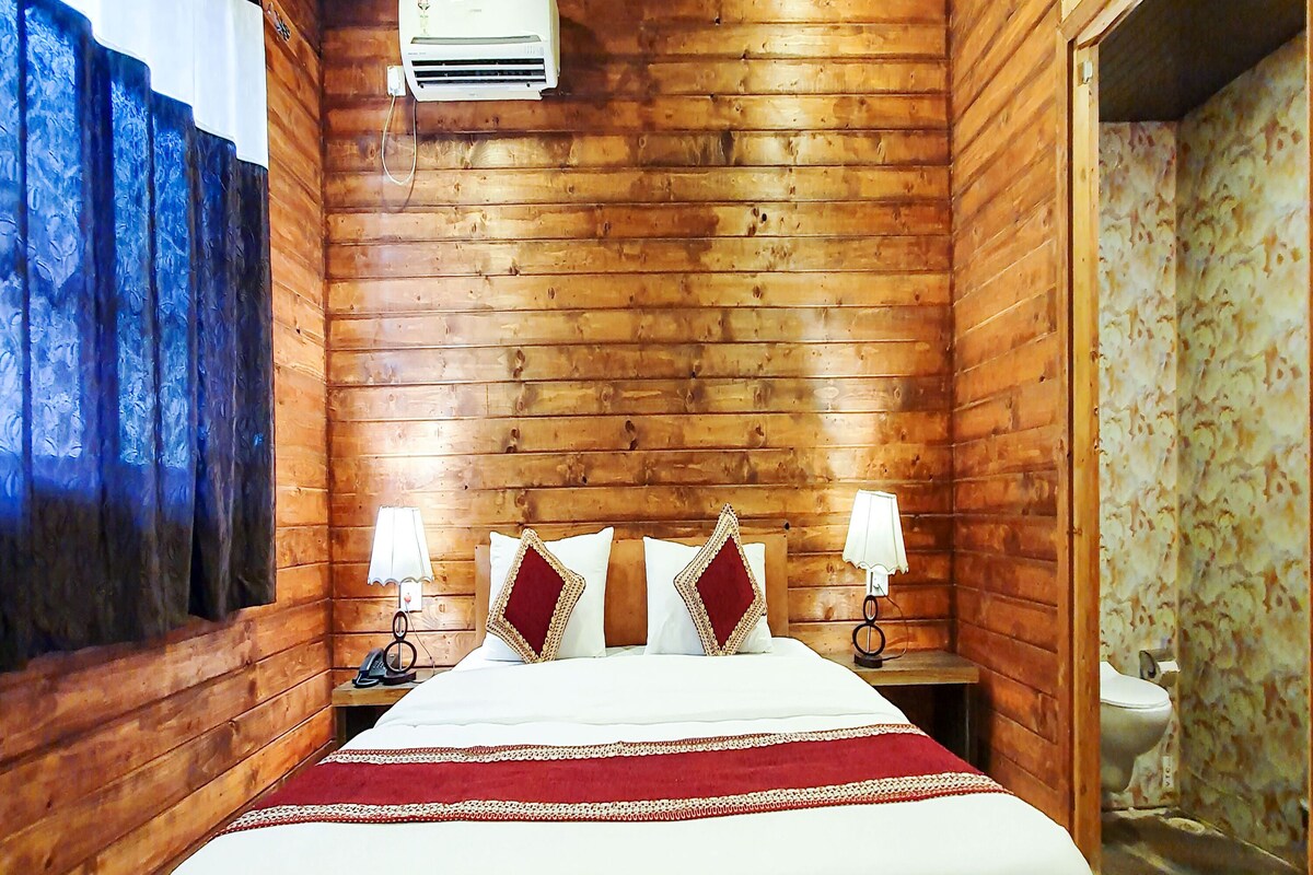 Quarto com painéis de madeira, uma cama, duas luminárias de apoio e um aparelho de ar condicionado.