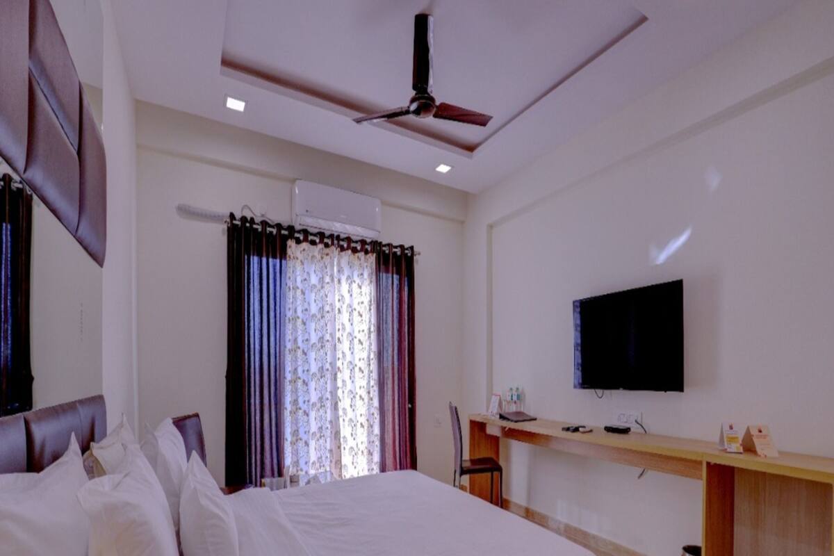 A bedroom with a bed, a desk, a chair, a television, and an air conditioning unit.