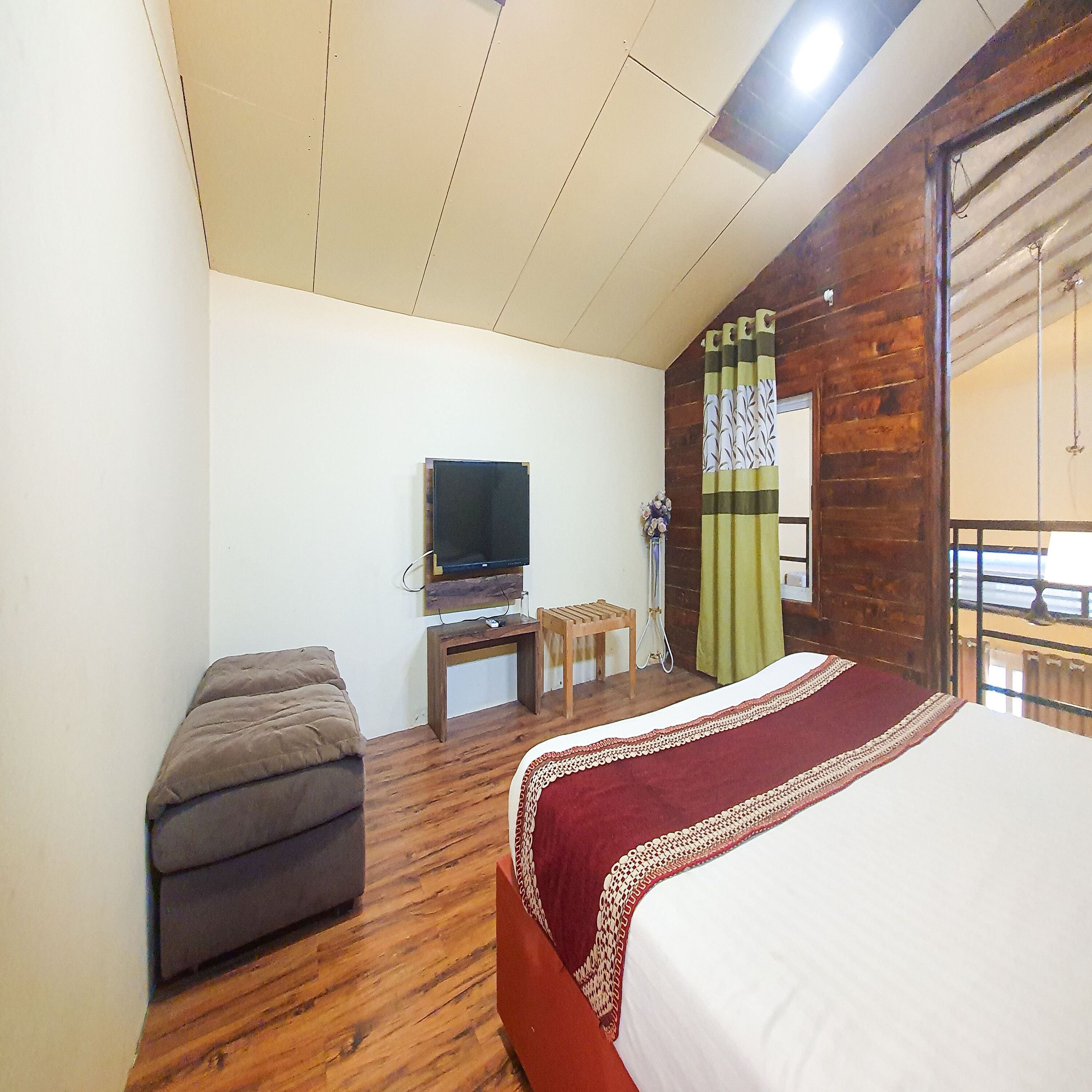 A bedroom with a bed, a television on a wooden stand, a small table, and a bench.