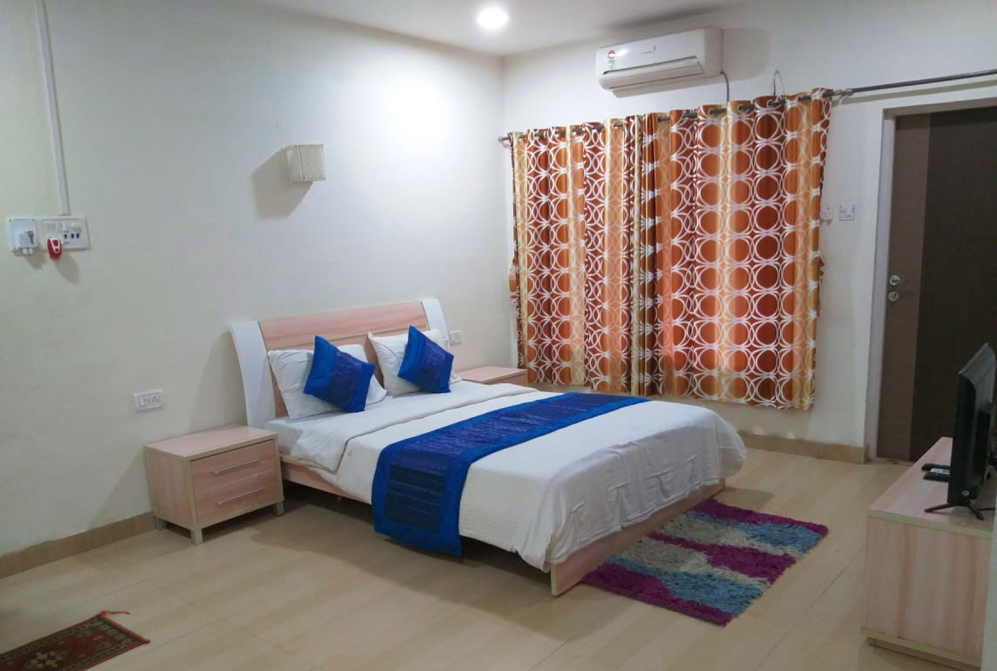 A bedroom with a bed, a nightstand, a television, and a patterned curtain.