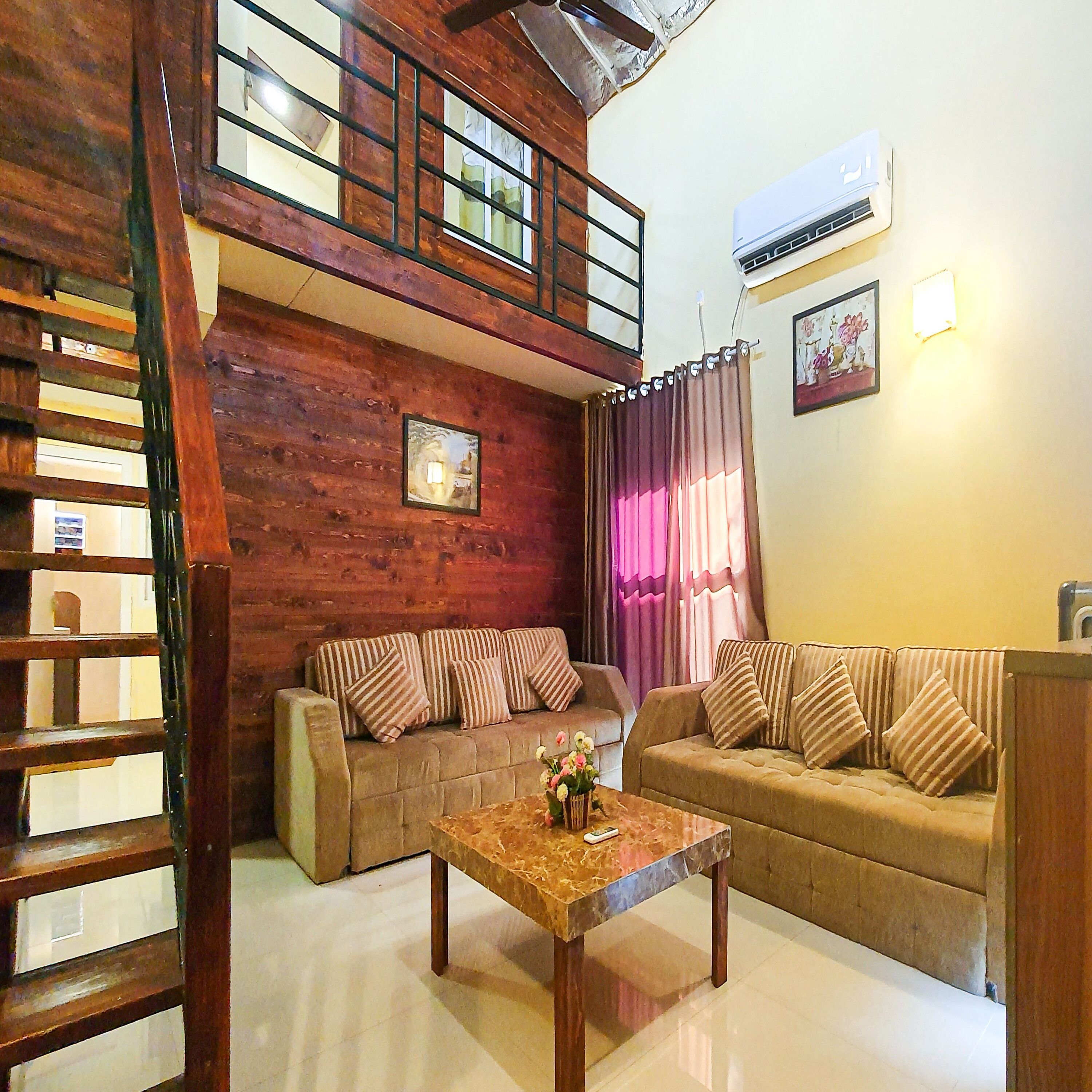 A living room with two sofas, a coffee table, a staircase, and an air conditioning unit.