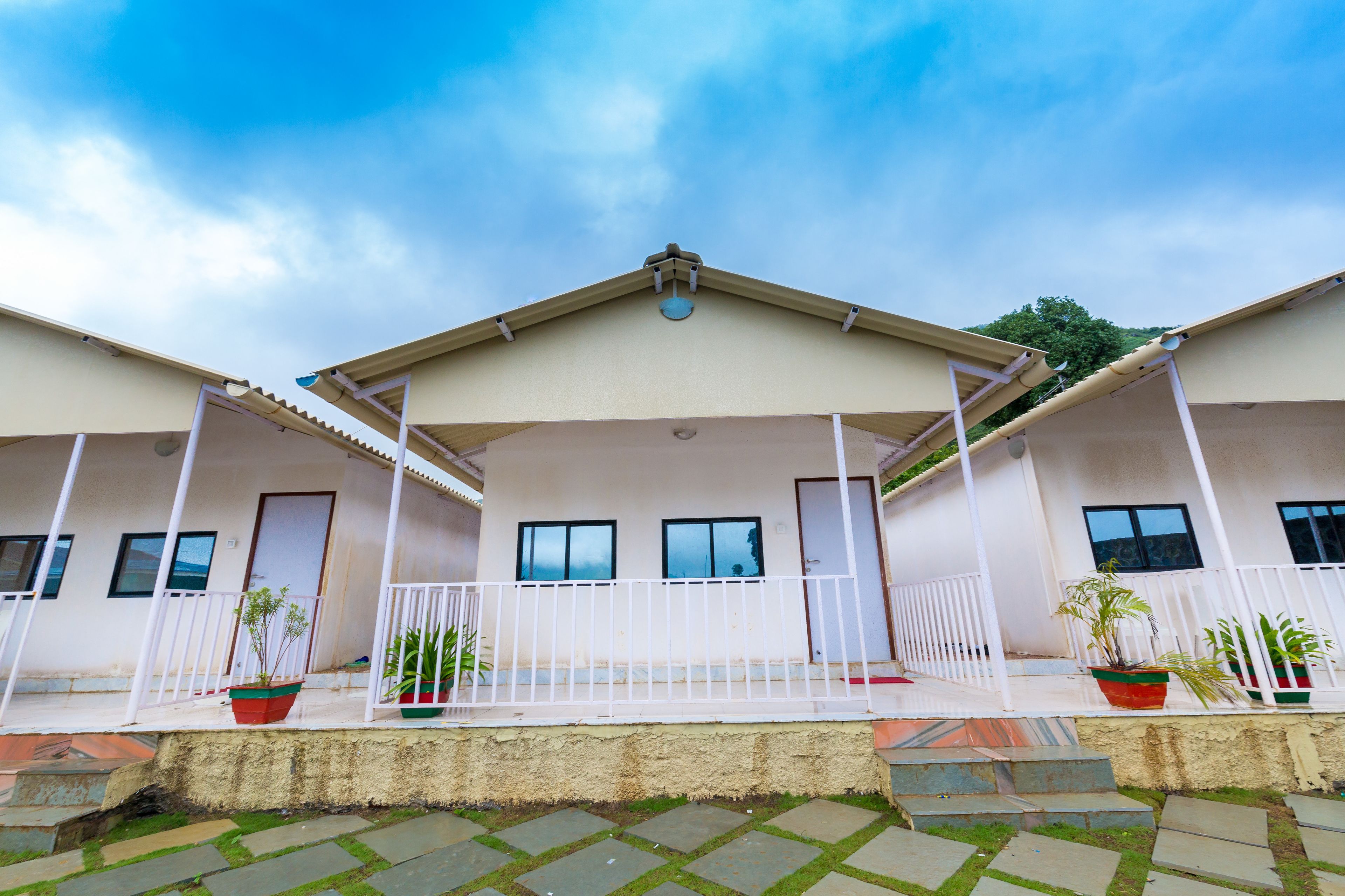 A two-story building with a flat roof and a balcony. There are potted plants on the balcony.