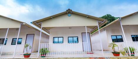 A two-story building with a flat roof and a balcony. There are potted plants on the balcony.