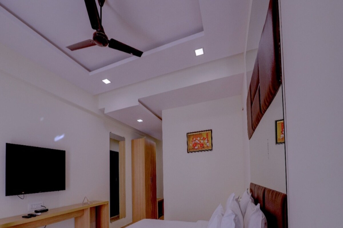 Quarto moderno com cama, TV de tela plana, ventilador de teto e cabeceira de madeira.