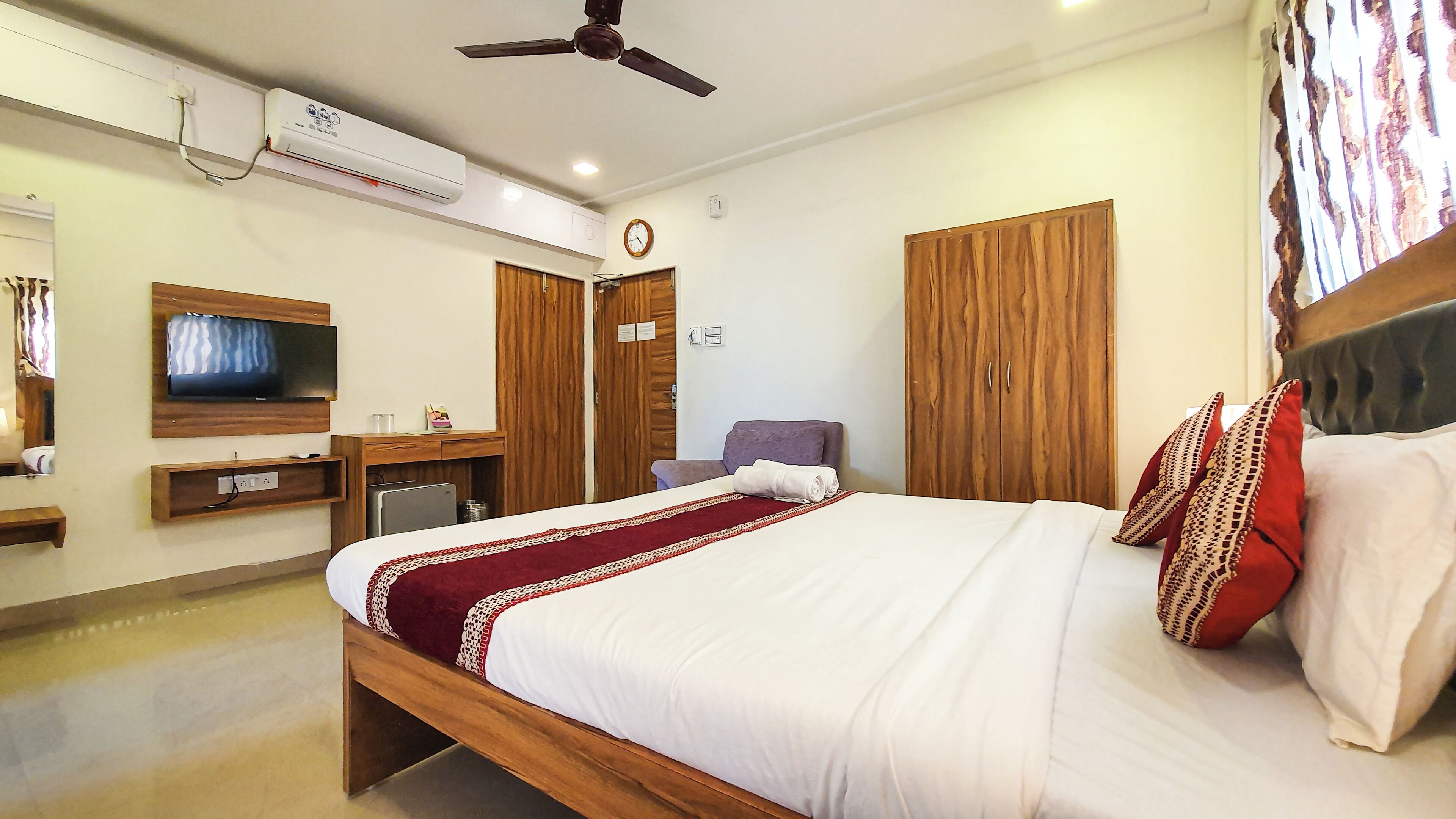 A hotel room with a bed, a TV, a wardrobe, a desk, and an air conditioning unit.